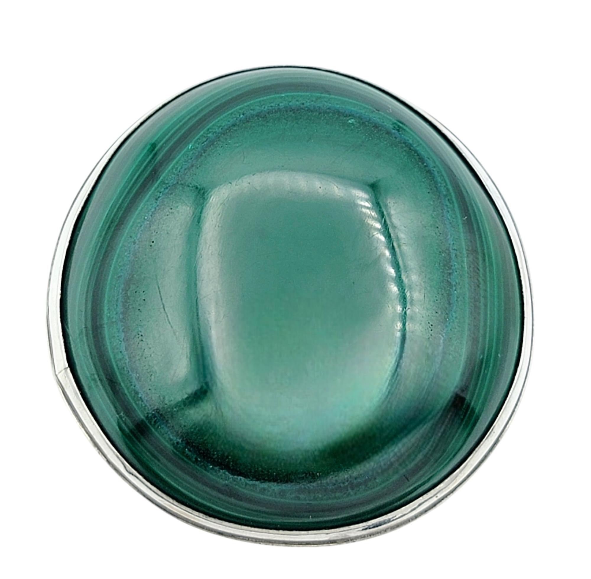 Misura dell'anello: 8

Entra in un mondo di bellezza naturale con questo sorprendente anello da cocktail, caratterizzato da un grande cabochon rotondo di malachite. Conosciuta per i suoi vortici ipnotici di tonalità verde intenso, la pietra
