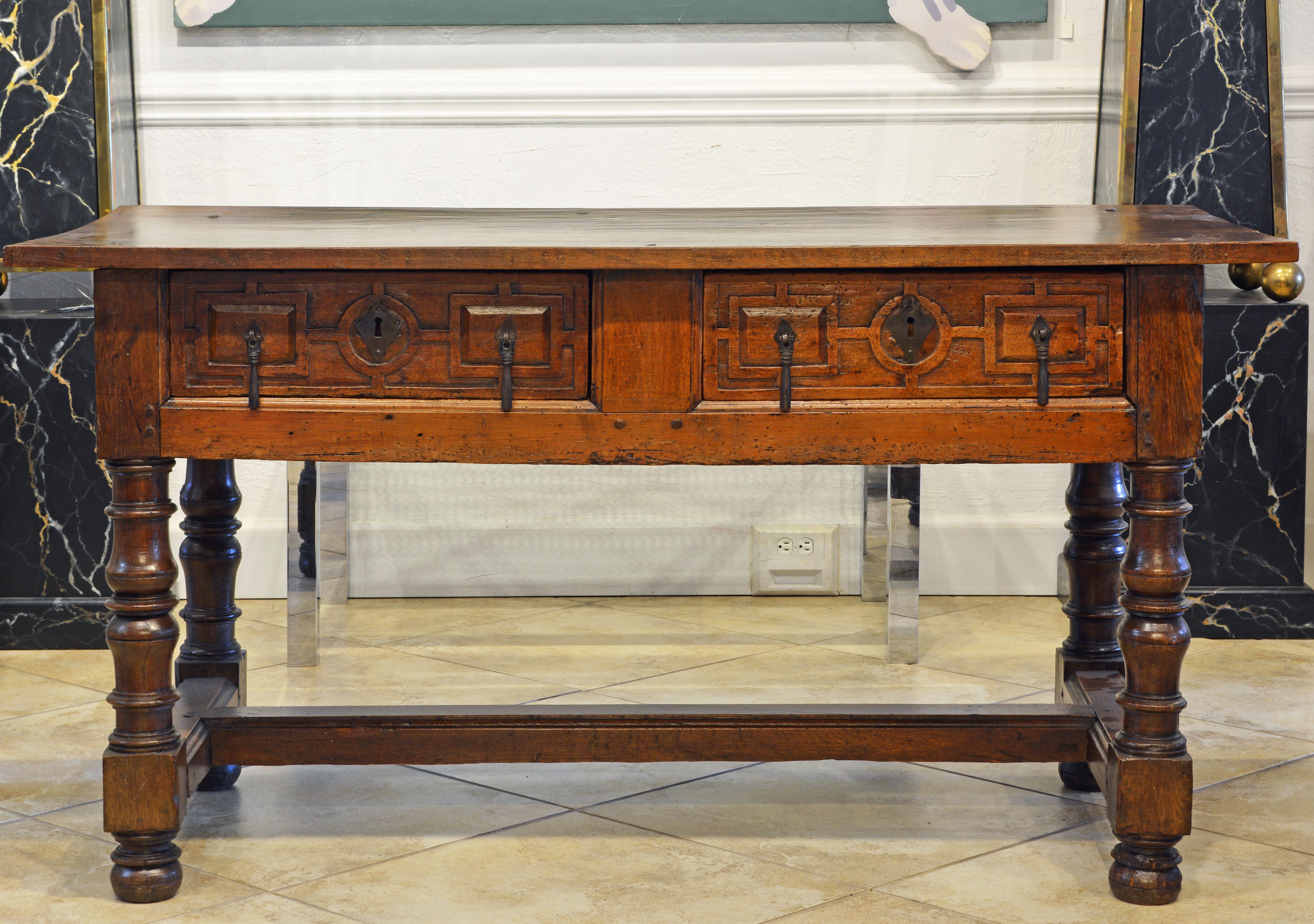 This excellent and impressive Renaissance table features a single board walnut top with visible nailheads above a carved oakwood frame holding two carved drawers with original hardware and resting on carved and turned legs united by low stretchers.