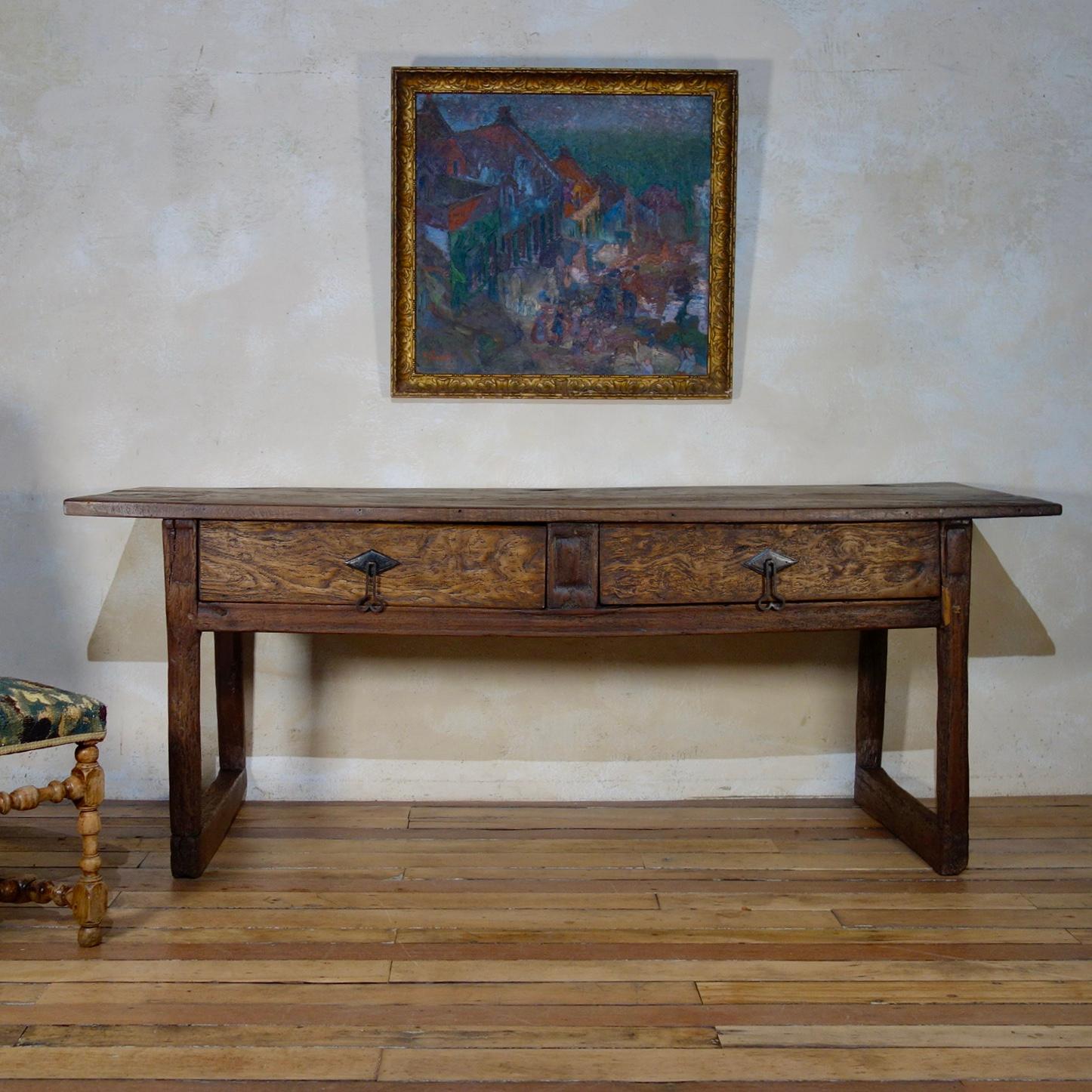 A Large scale late 17th century chestnut Spanish Iberian serving table. 
Demonstrating a single rectangular planked top above two frieze drawers displaying later replaced forged iron drop handle. 
 
Raised on chamfered corner supports united by