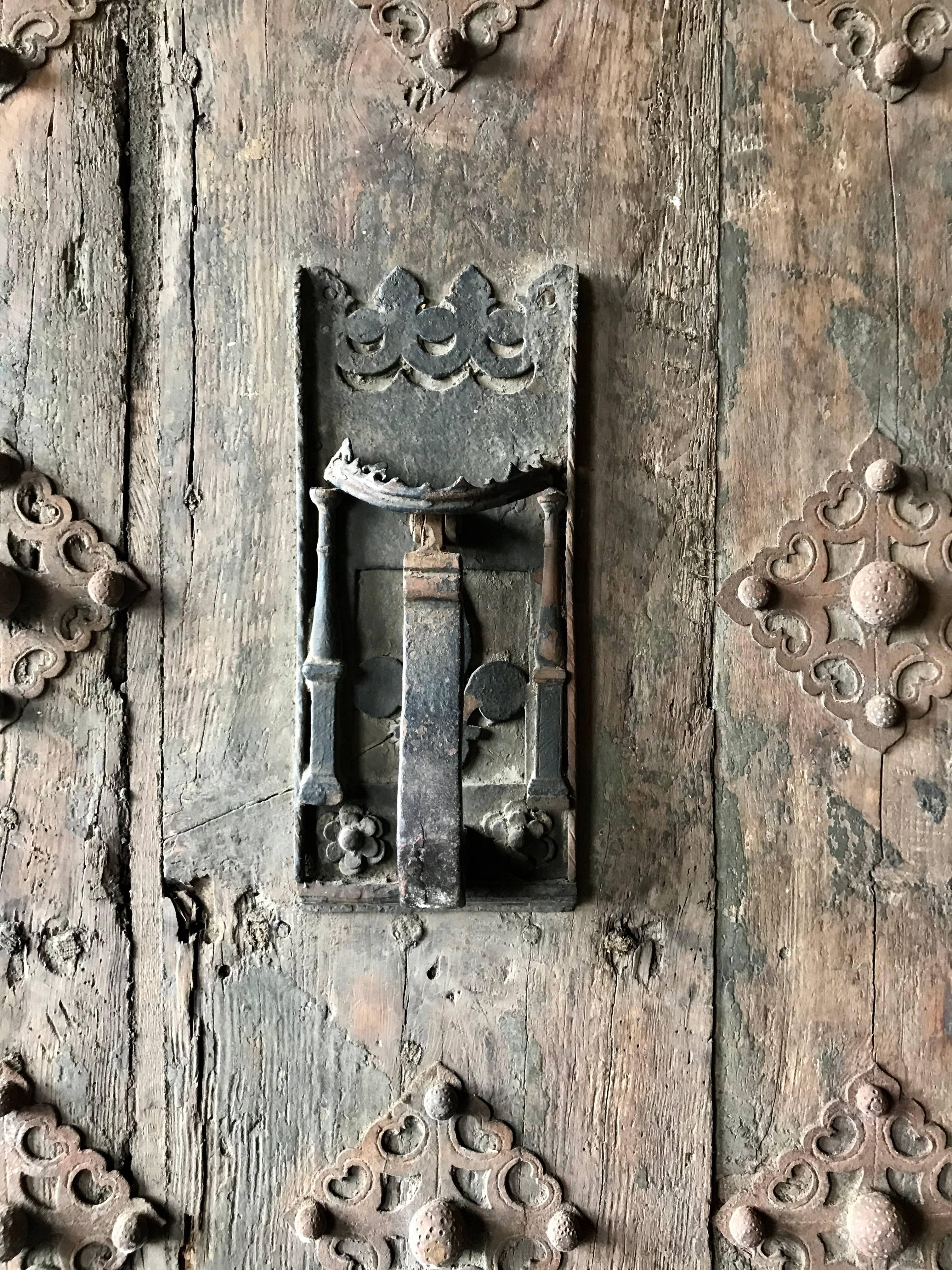 Antique heavy exterior chestnut wood door from the Catalan region of Spain with it's original hardware, knocker and iron decorative implements, rustic original condition, amazing patina color, finish and surface. Hand delivery avail to New York City