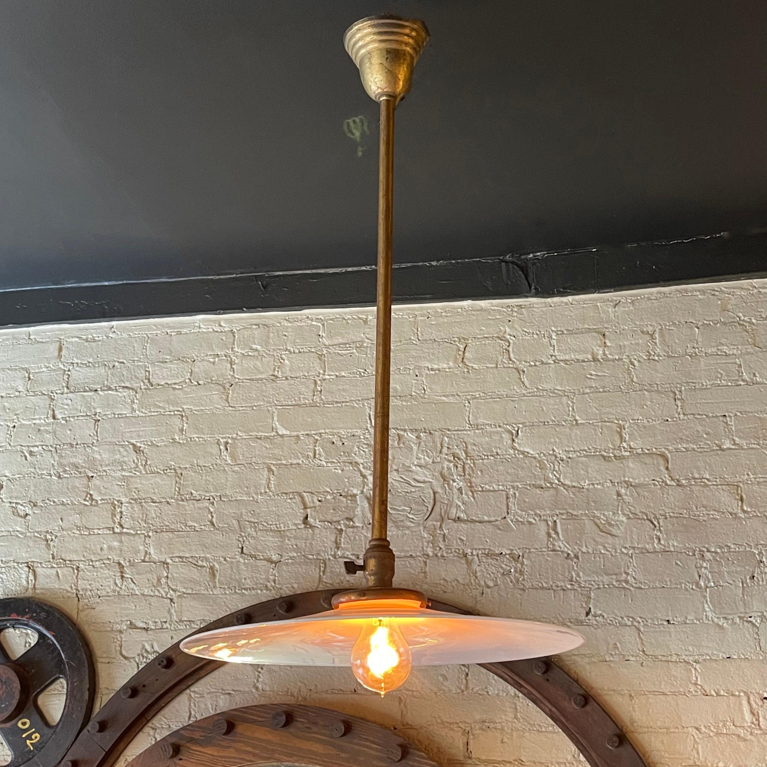 Early 20th century, industrial pendant light features a large 18 inch diameter, opaque, milk glass disc shade on a patinated brass pole with brass canopy and paddle switch hardware.