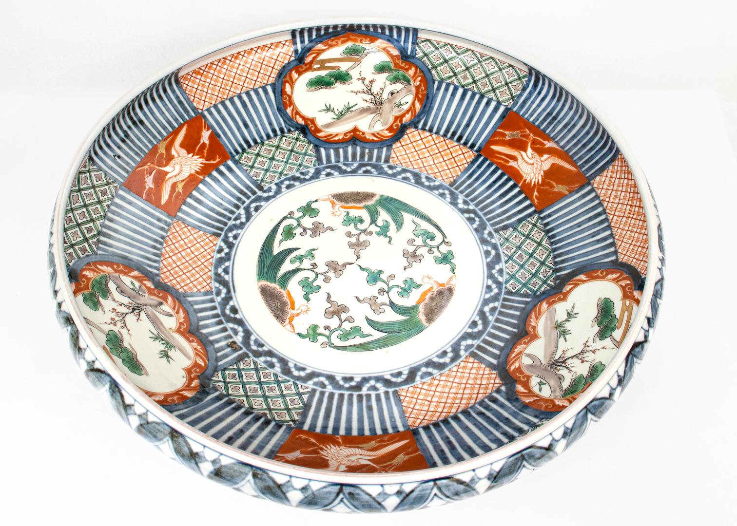 A fine Japanese Imari porcelain bowl.

In a very large, low walled form.

With typical blue underglaze decoration and red, salmon, green, and brown cold-painted decoration throughout.

The bowl is slightly out-of-round and the side walls vary