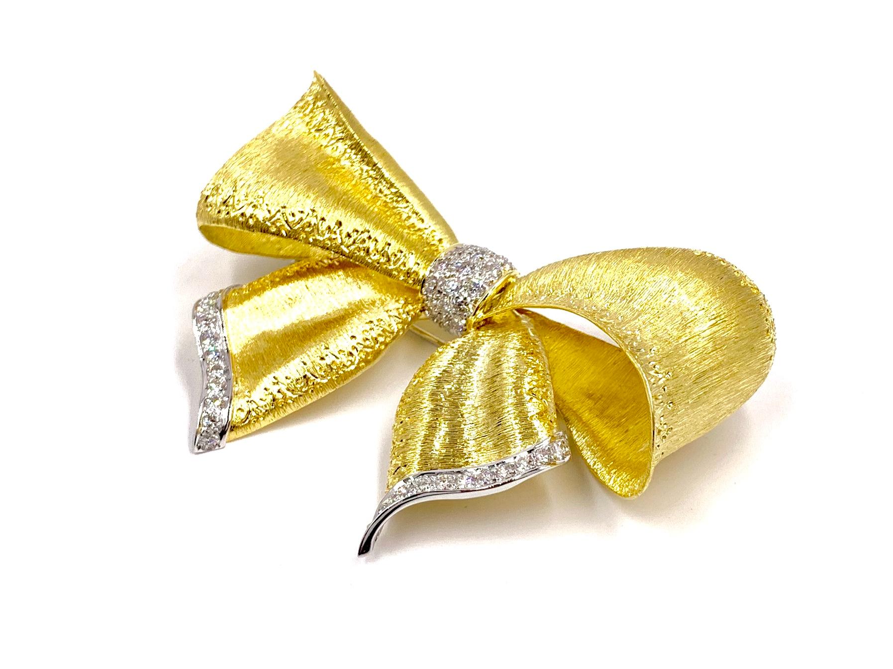 An elegant 18 karat yellow and white gold bow brooch with a gorgeous hand etched florentine finish and featuring 1.65 carats of bright white round brilliant diamonds. Diamond quality is approximately F color, VS2 clarity. Diamonds are set in white