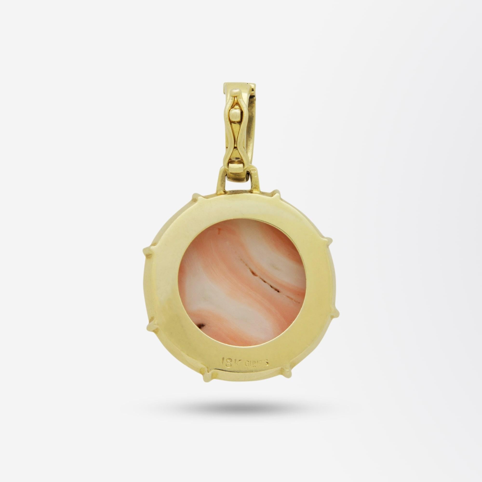 A bold 18 karat gold, coral and diamond pendant enhancer by Gumps. The pendant centres on a round cabochon piece of angel-skin coral which is framed in yellow gold with a border of polished gold interspersed with panels of grain set brilliant cut