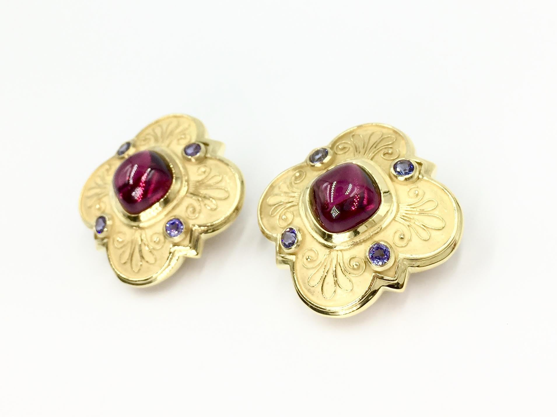 Made with superior quality by Seidengang. These 18 karat yellow gold clover earrings are made in a unique 'barbed quatrefoil' clover shape mixing both brushed and polished gold for dimension. Center is set with a vivid cabochon reddish-pink