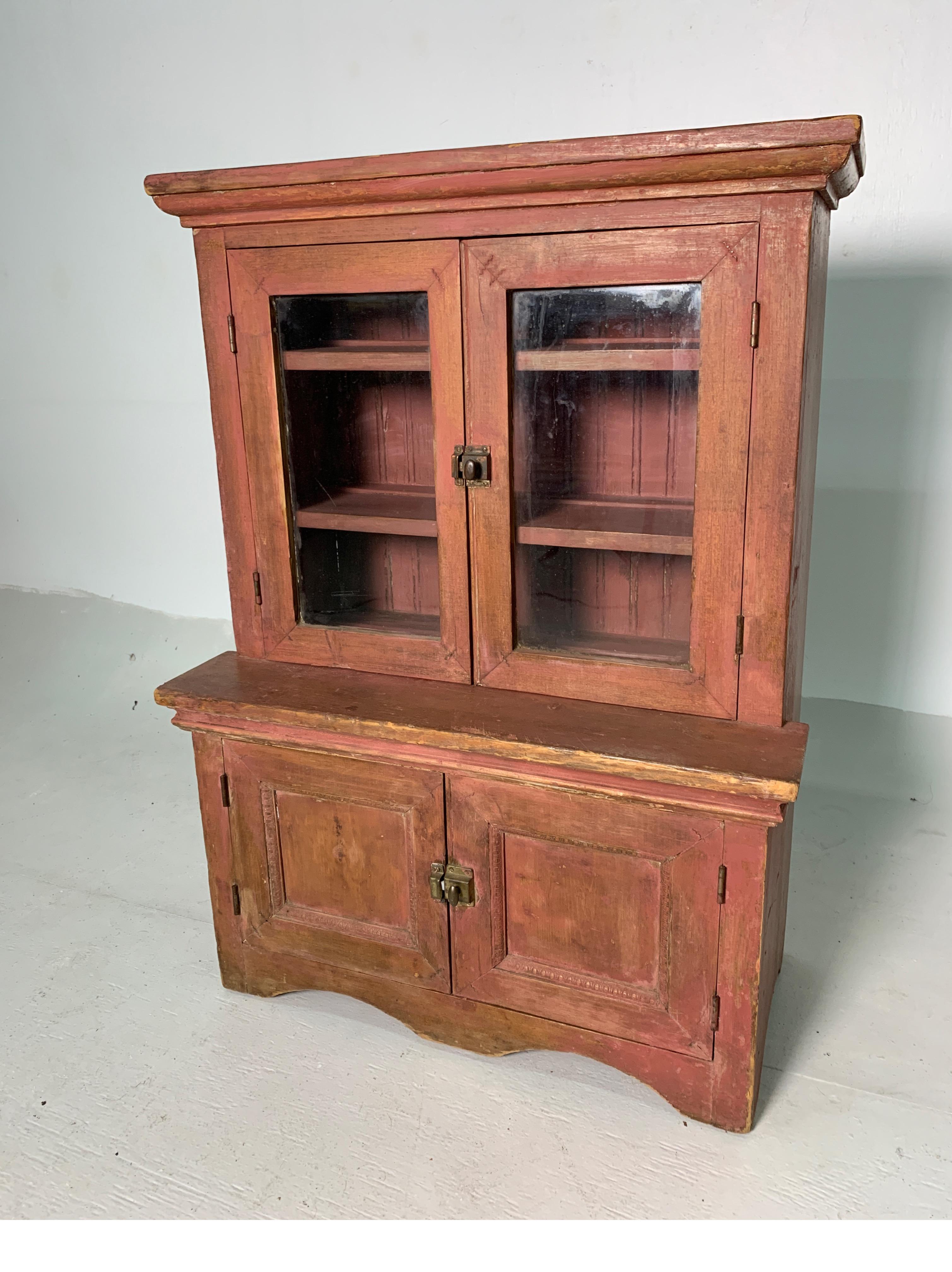Large, child's wooden cupboard with glass-pained doors and lower cabinet, older brick dust paint finish and original hardware.