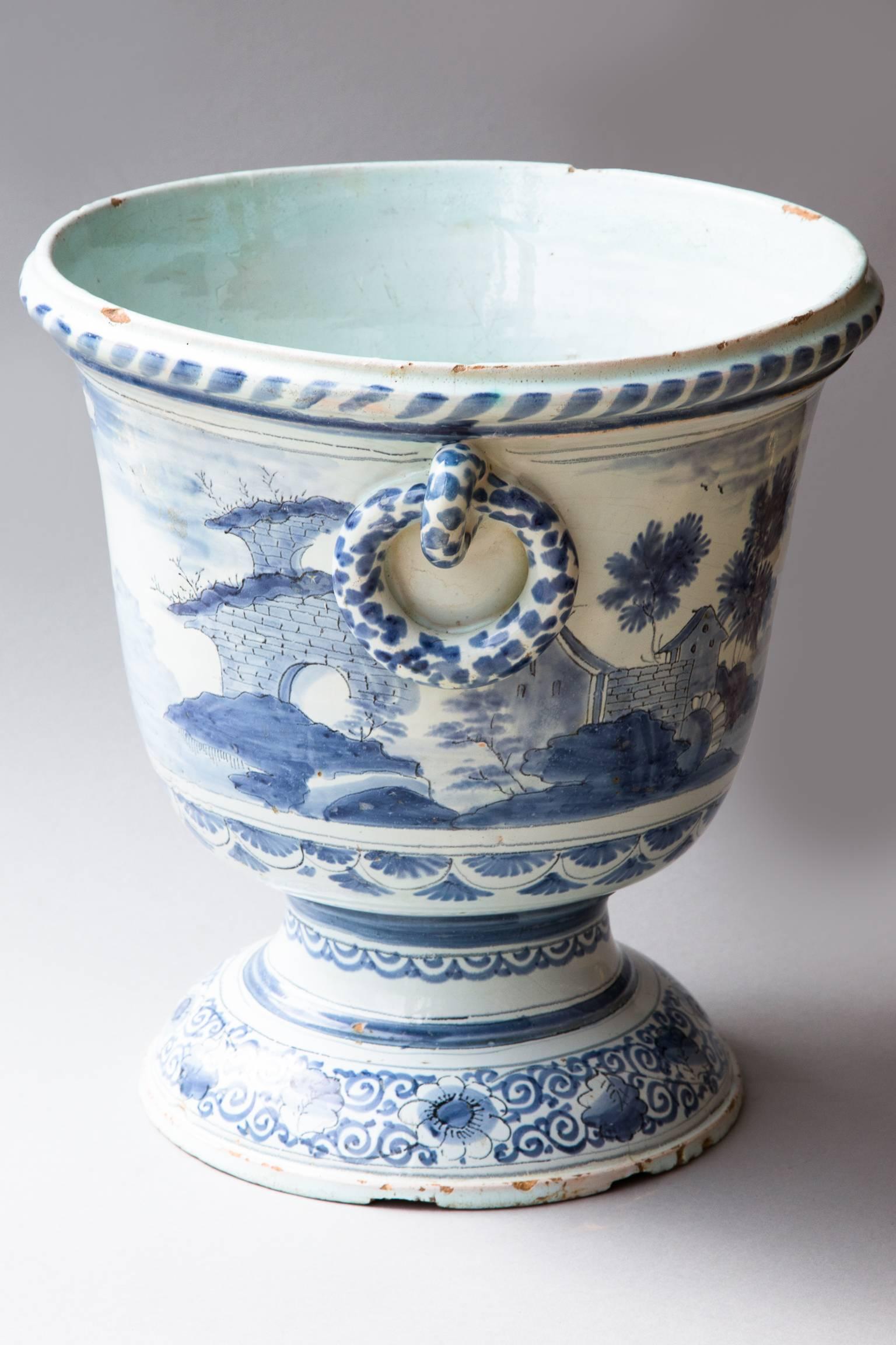 Large glazed faïence cache pot decorated in camaïeu bleu with pastoral scenes. Handles moulded in the shape of rings and raised on a plinth base decorated with geometric patterns and flowers.
Nevers, France, circa 1760.
Some old restoration, the