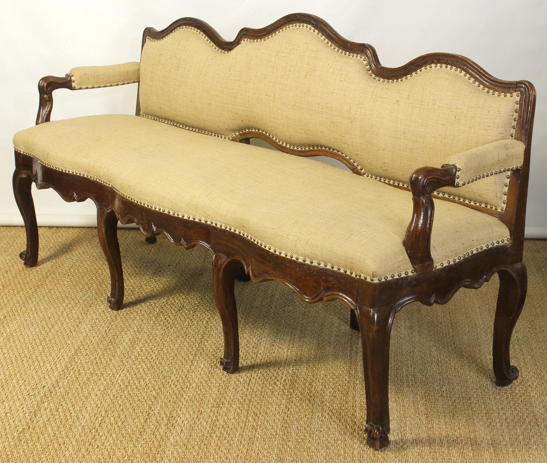 An exceptional and beautifully proportioned late 18th century. Italian carved walnut bench recently upholstered in a natural linen burlap fabric accented with brass nail heads.