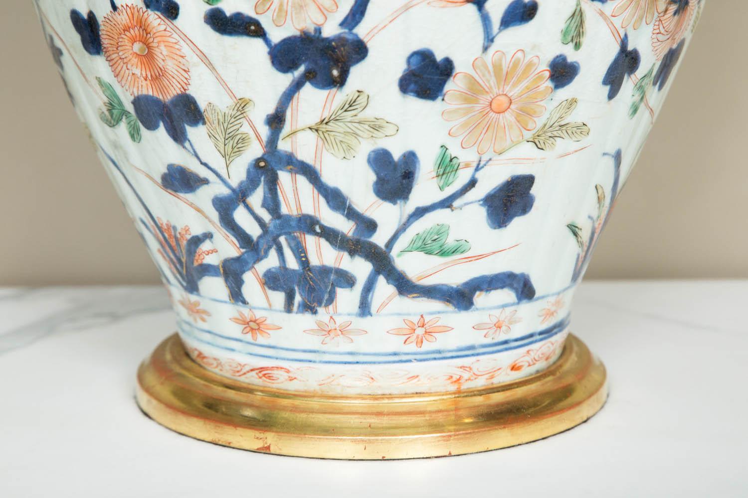 A beautifully decorated 18th century Japanese Imari vase featuring scrolling flowers on a white background.
Condition: 2 faint hairline cracks running through the body and a small chip professionally restored at the neck.