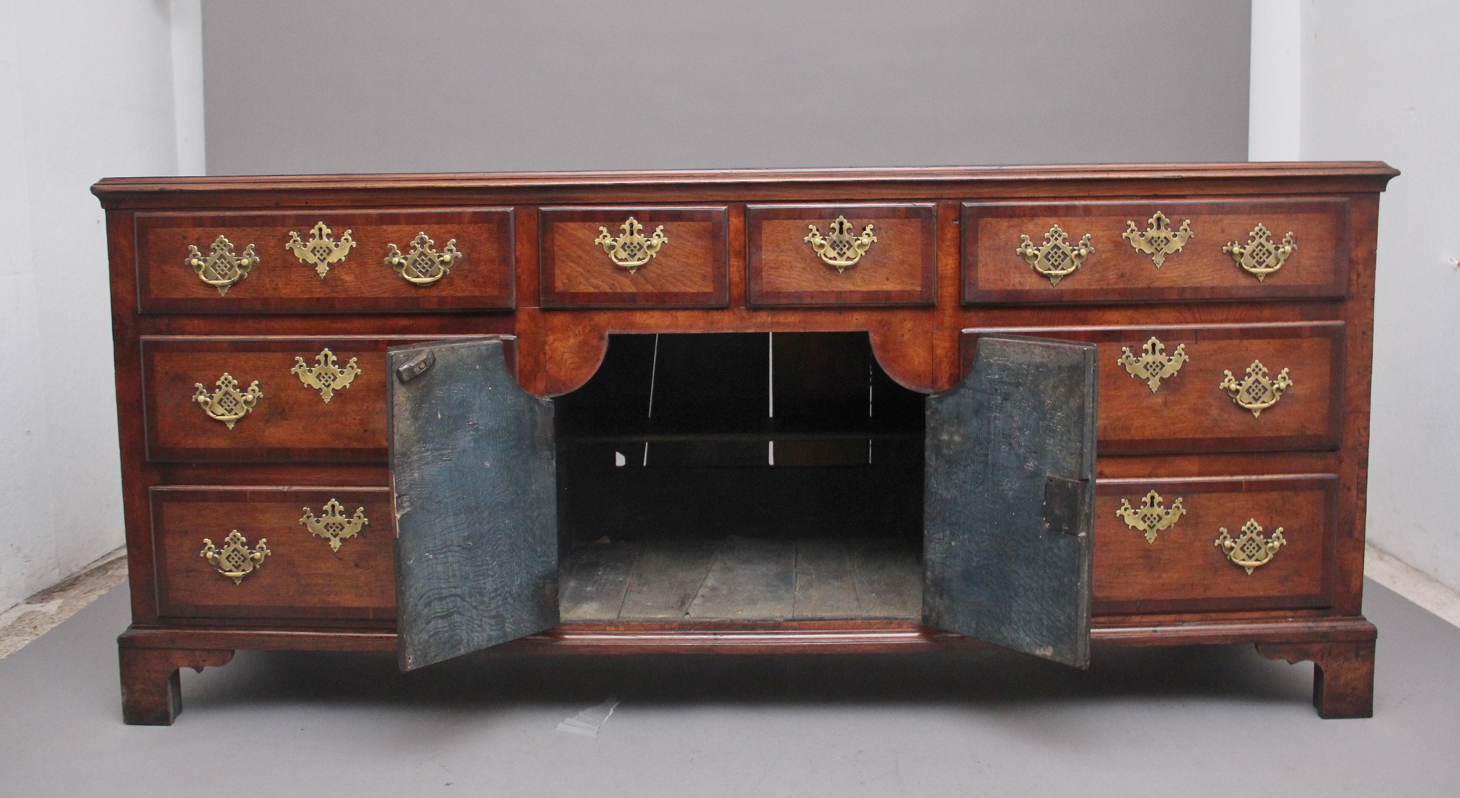 18th century oak dresser, the moulded crossbanded top above a selection of eight graduated drawers with crossbanded drawer fronts and pierced brass fret handles and escutcheons, two shaped cupboard doors at the center with a workable lock, supported