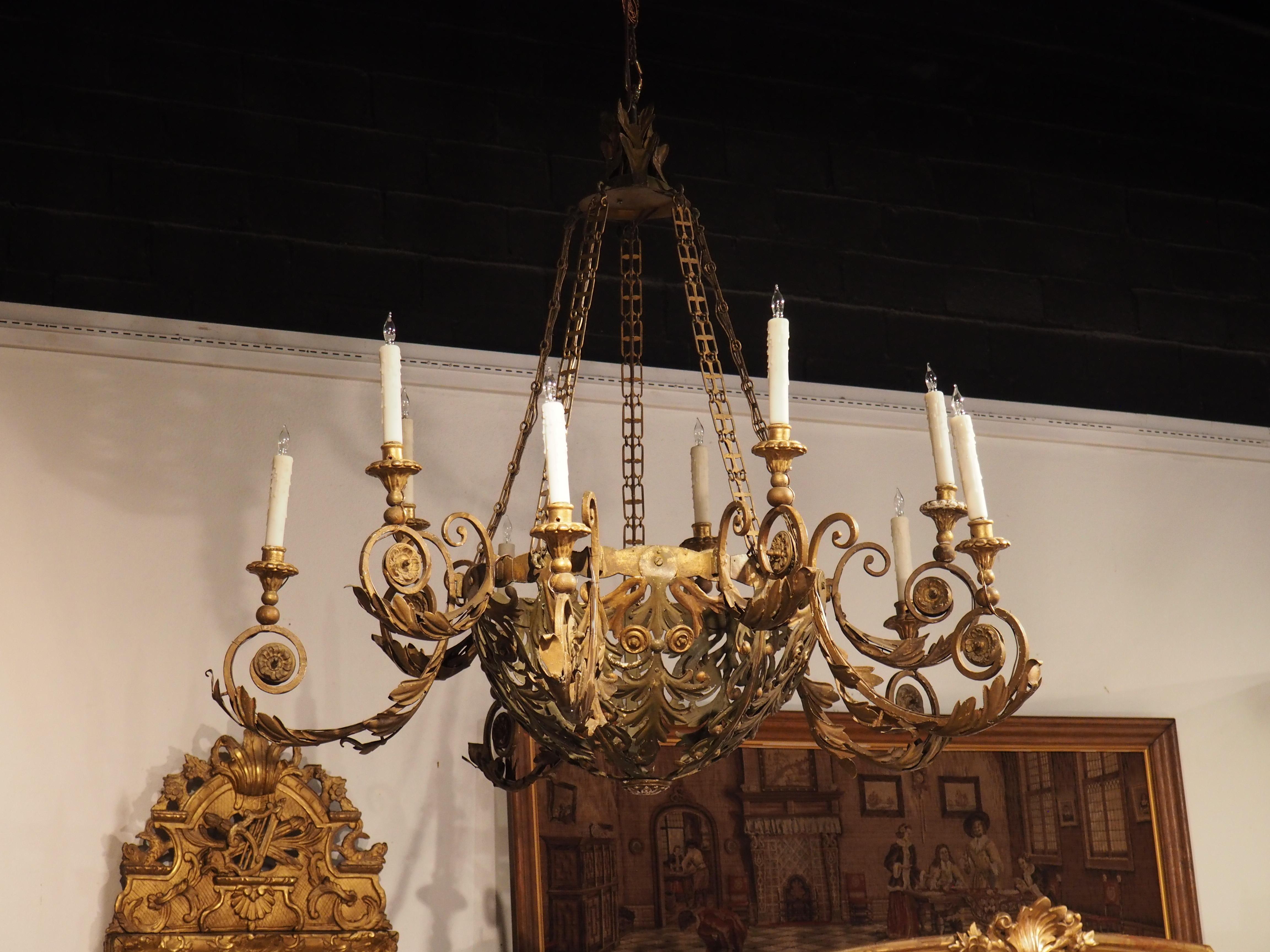 This sprawling Italian chandelier features a large open bowl adorned with parted leaf margents painted in olive green with gold highlights. The margents trail down to the bottom of the bowl, where they join a wooden rosette painted in gold. 10