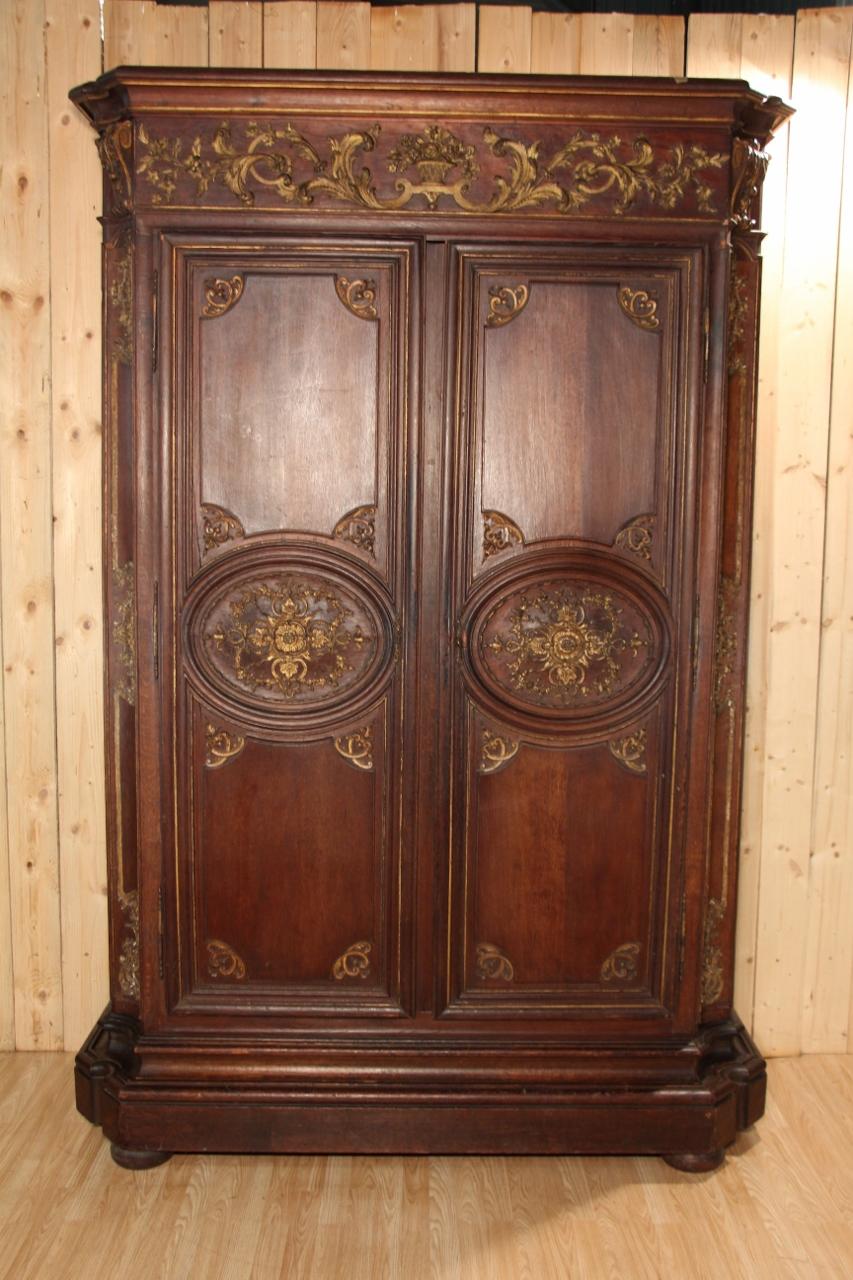 A straight-cornice wardrobe with two doors and a false frame, made of molded oak with carved and gilded decoration of foliate scrolls, flowers and finials, arched uprights. Parisian work from the Regency period, in good condition, with some minor