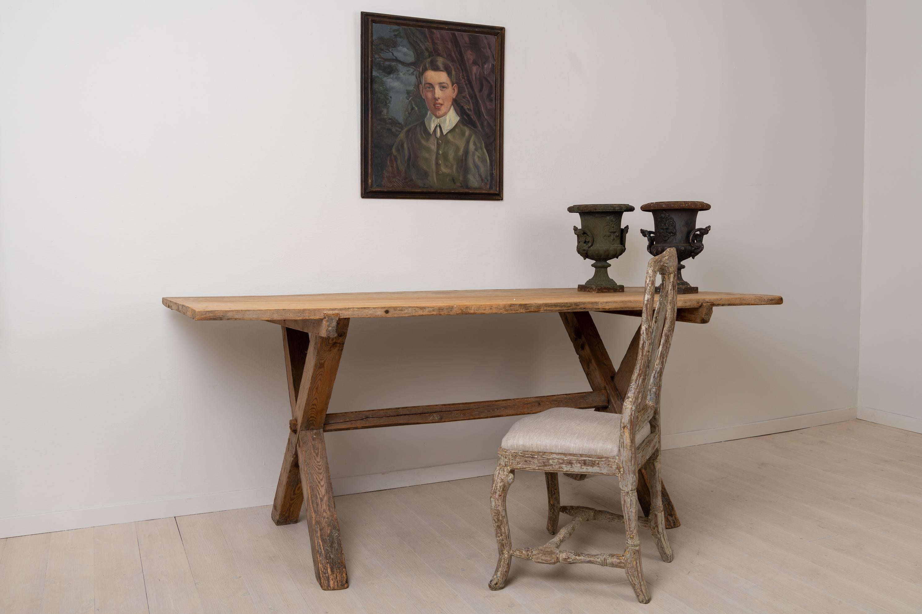 Large Swedish pine table from the late 1700s. The table is rustic and primitive with clean and lightly patinated surfaces on both the table top and X-base. The table top consists of two large boards and is detached from the legs. Underneath the