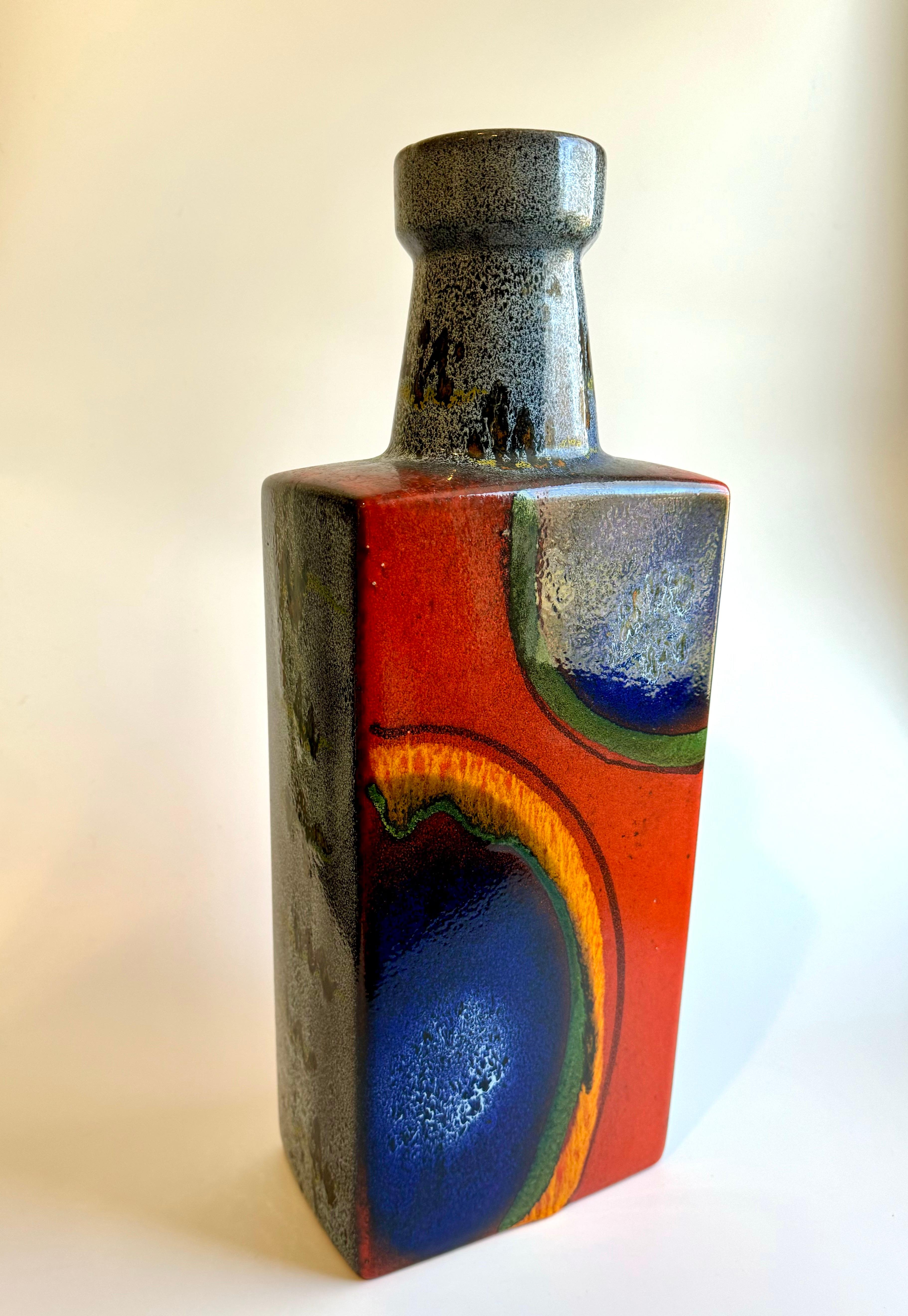 Es handelt sich um eine große westdeutsche Vase der Firma Scheurich Keramik, die Mitte des 20. Jahrhunderts zu den größten Keramikherstellern gehörte. Die Vase hat eine unverwechselbare Glasur mit einer kräftigen Farbpalette, die Orange, Blau und