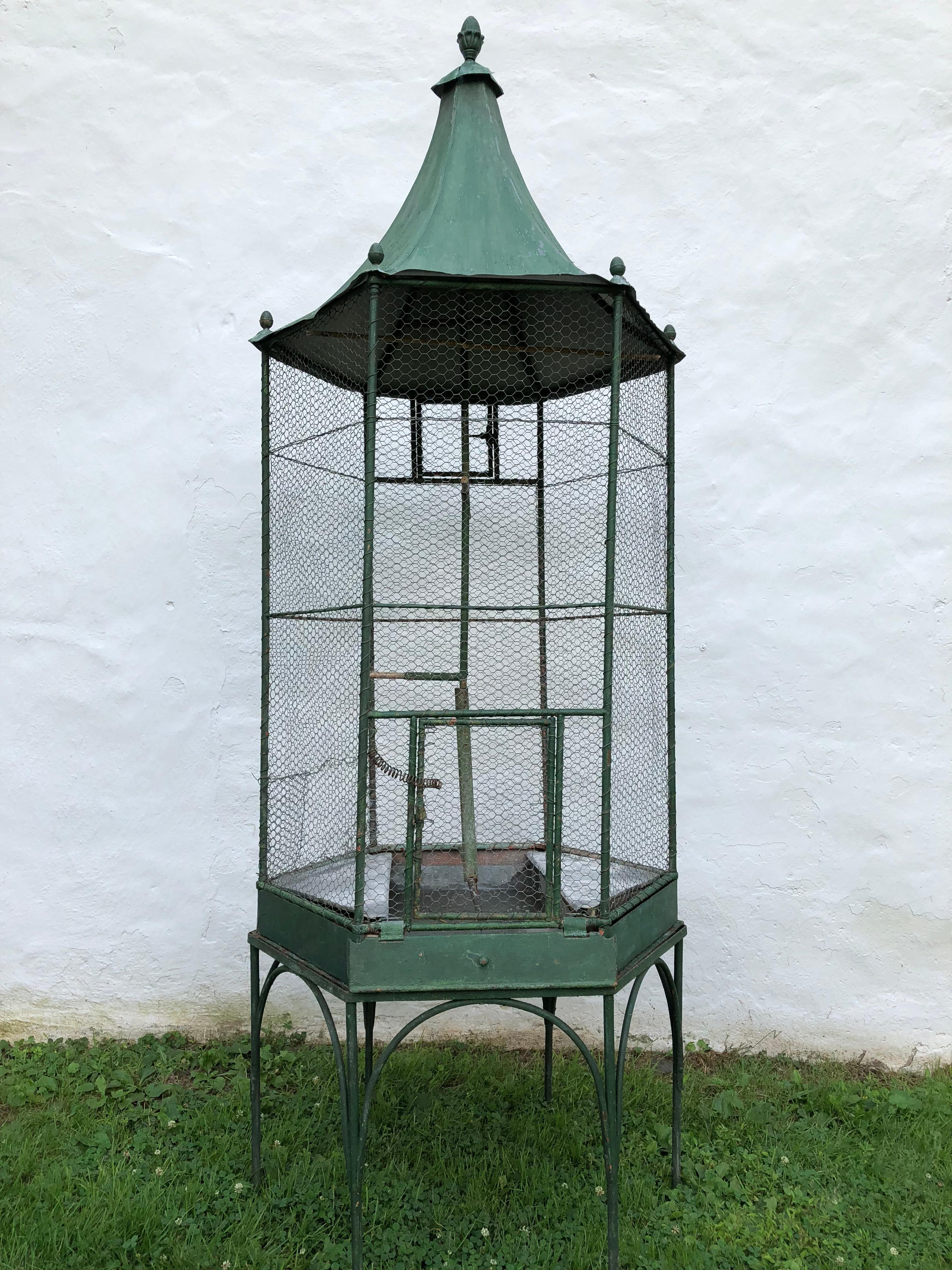 A stylish Hollywood Regency, 1920s green painted zinc and steel parrot cage on stand with zinc liners and a central perch. Its six sided and has a pagoda style roof with an acorn finials can be used indoors or out.