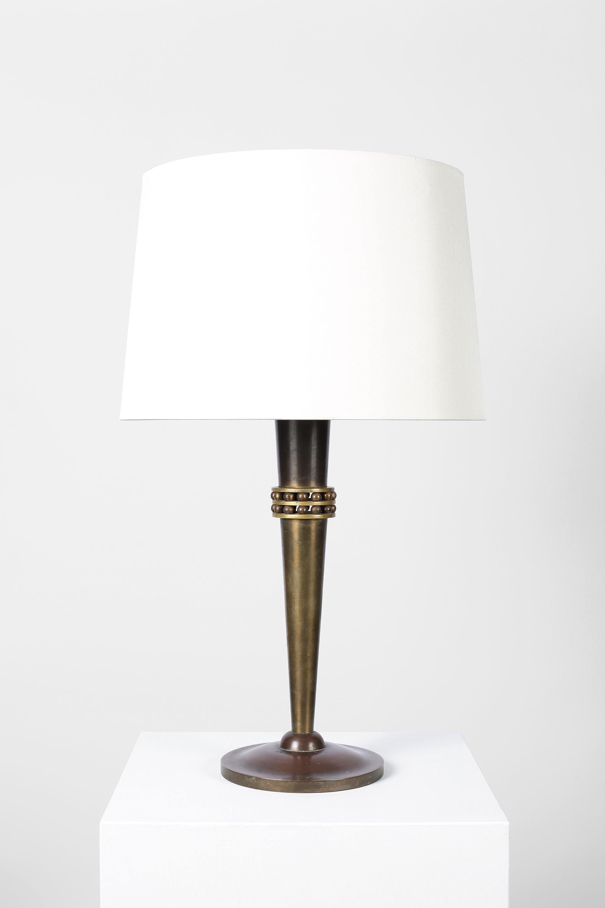 A large, fine patinated bronze table lamp with tapering stem decorated with two rows of spheres. French, c. 1930s. Supplied with a tapered off-white dupion silk shade.