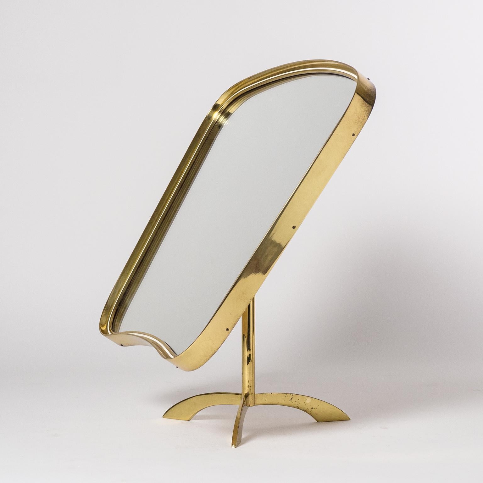 Rare large brass vanity or table mirror from the 1950s. Tripod base with and unusually large and organic shaped mirror. The continuous brass frame is approximately 1 inch thick and nicely profiled with a thin off-white enamel. The backplate is made
