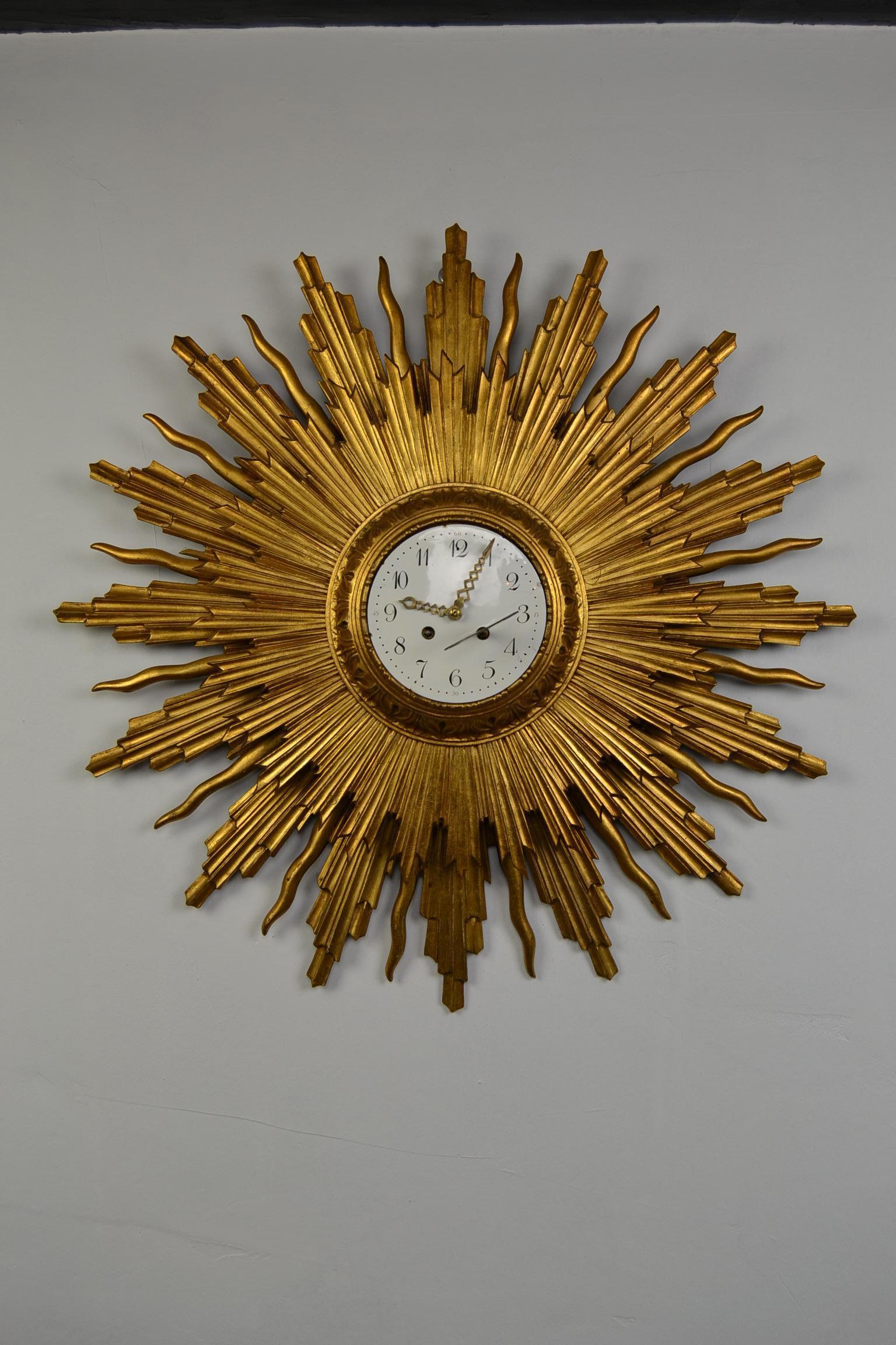 Stunning large sparkling giltwood sunburst clock.
Diameter: 30,32 inch - 77 cm !! 

This vintage sunburst clock from the 1950s is made of a gilt wooden frame, consisting of two layers. 
It has an enamel or porcelain dial, copper pointers and a