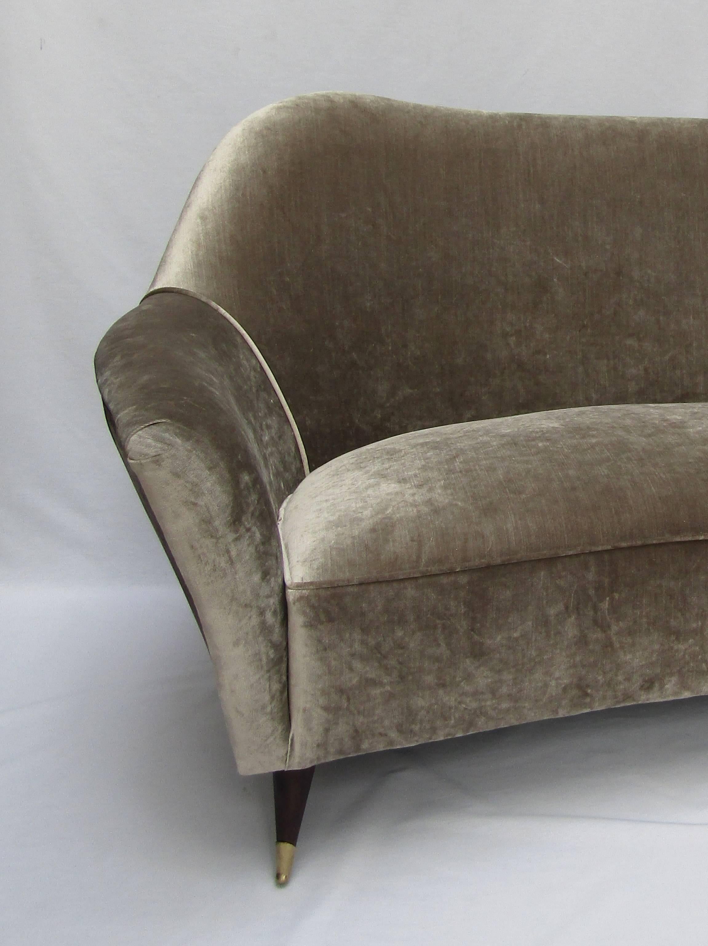 A large curved three-seat sofa with wooden legs and brass sabots
Upholstered in designers Guild Glenville velvet color 'Pebble'
Vintage cushions sold separately.

Measures: Height 35 in / 89 cm
Width 83 in / 211 cm
Depth 34 in / 86 cm.
 