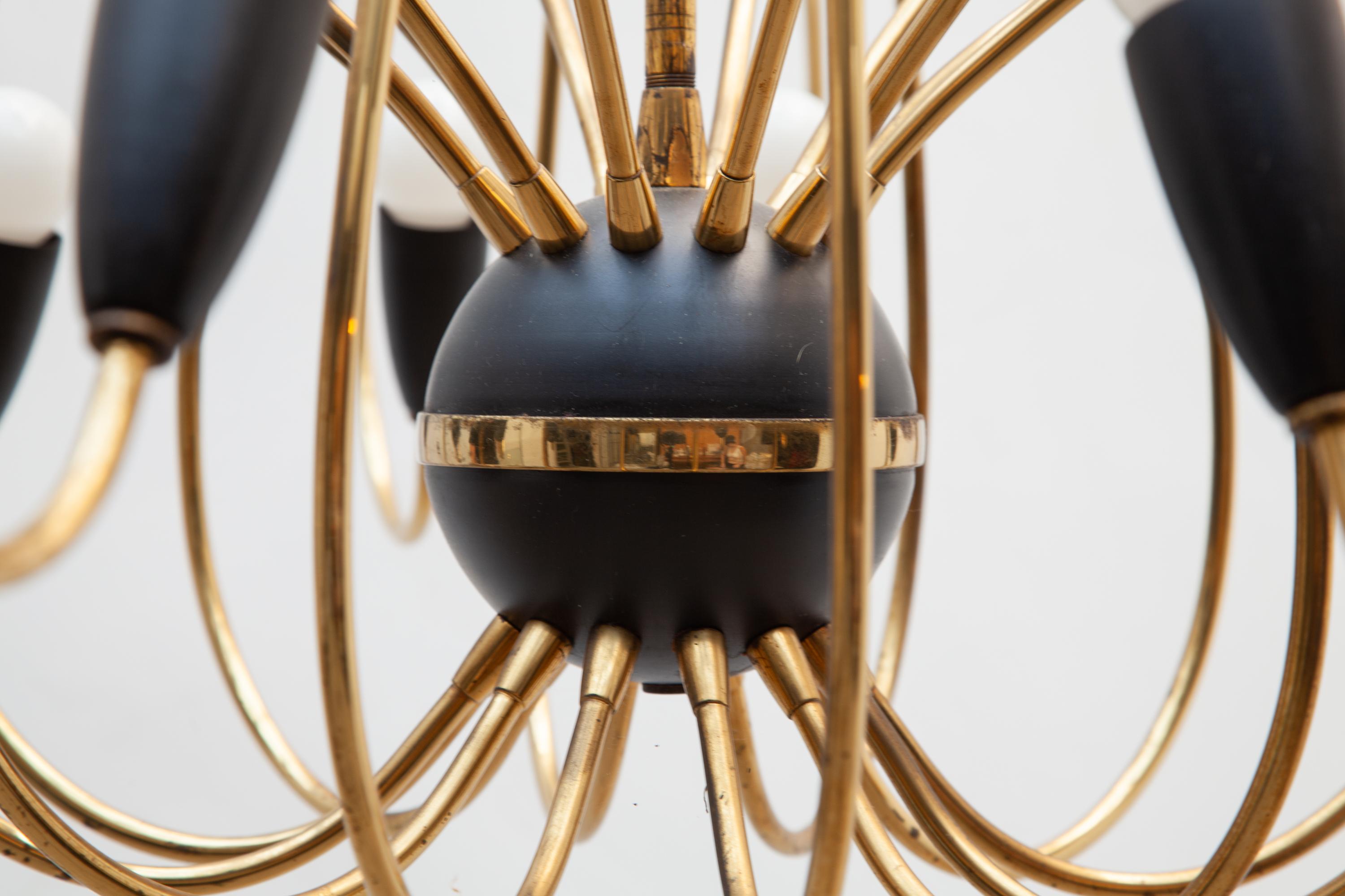 Vintage Mid-Century Modernist sputnik chandelier with twenty-four arms in the style of Stilnovo.
Dramatically swing curved brass with black bakelite fluted lamps connected from a black enameled central ball. Lit by 24 bulbs. 
