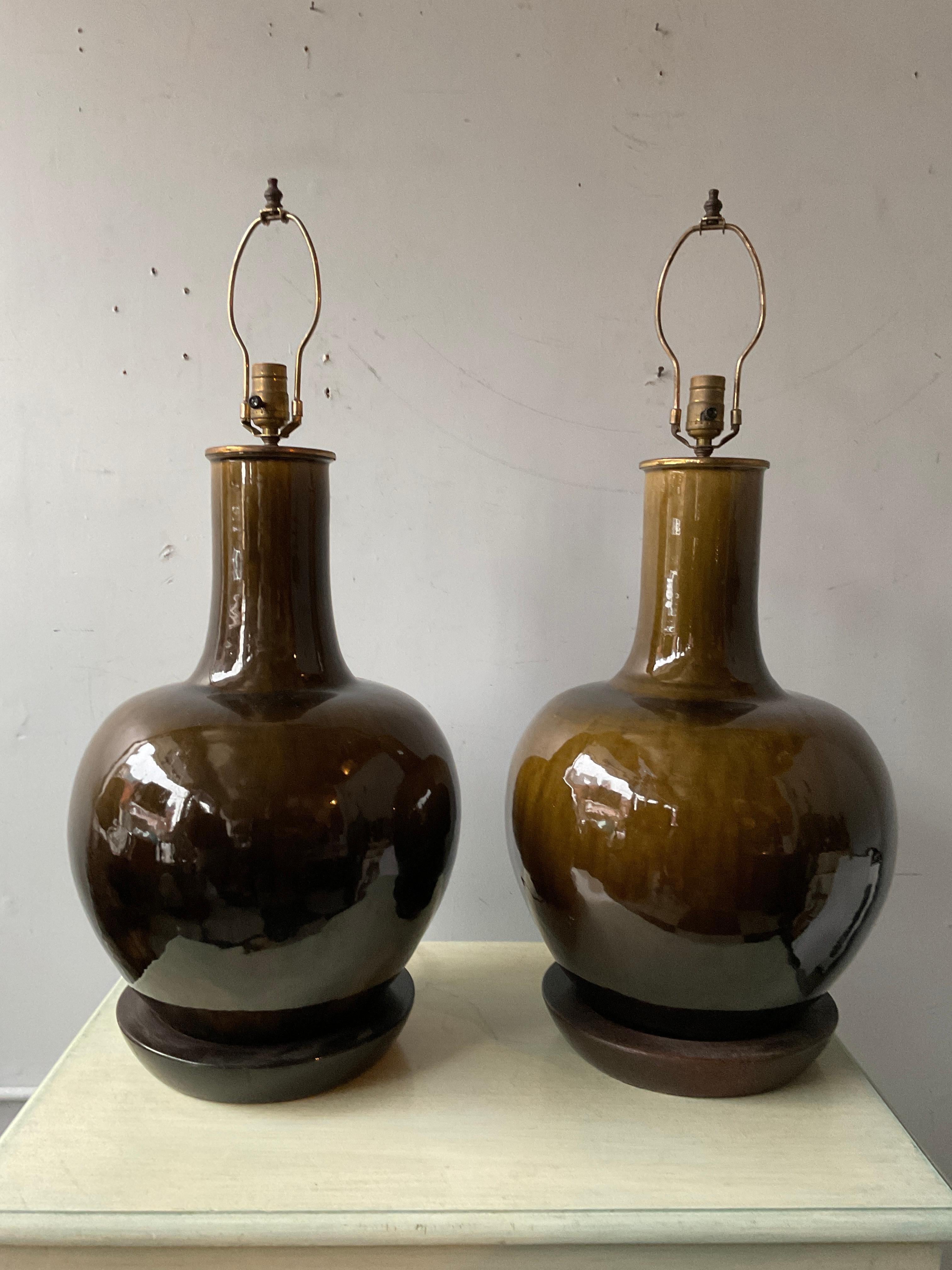 Pair of 1950s large  chunky Thai ceramic glazed ginger jar lamps. Brass top caps.   Wood bases. Height  of 25” is to top of socket.
Lamps need rewiring.
Wood bases need refinishing as shown in last picture.