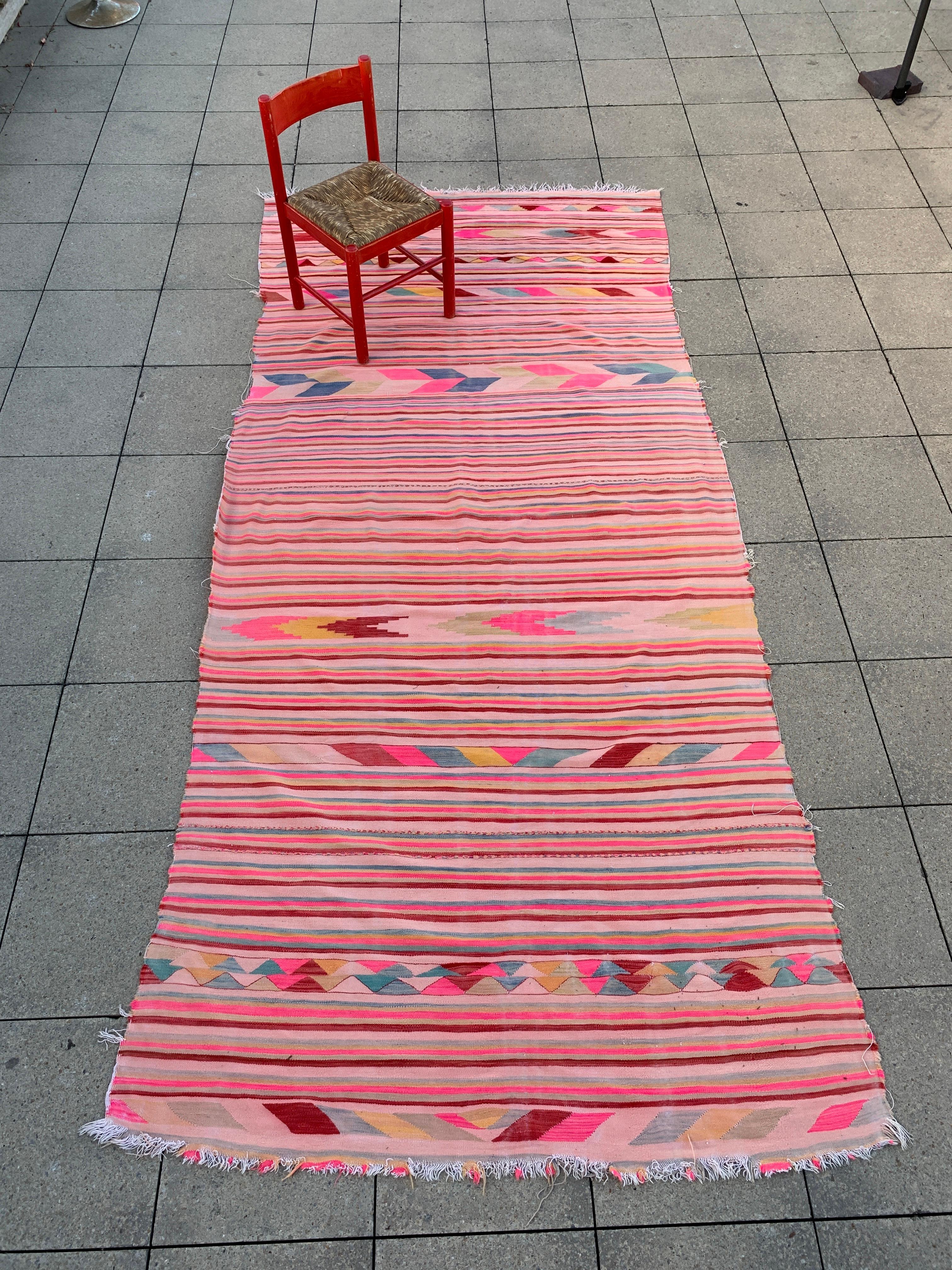 Explore the heritage of North African craftsmanship with this vintage Berber rug from 1960s Algeria. Featuring long, striped patterns and occasional diamonds and arrows, this unique piece is set on a light pink base.

The rug's dominant hot pink,