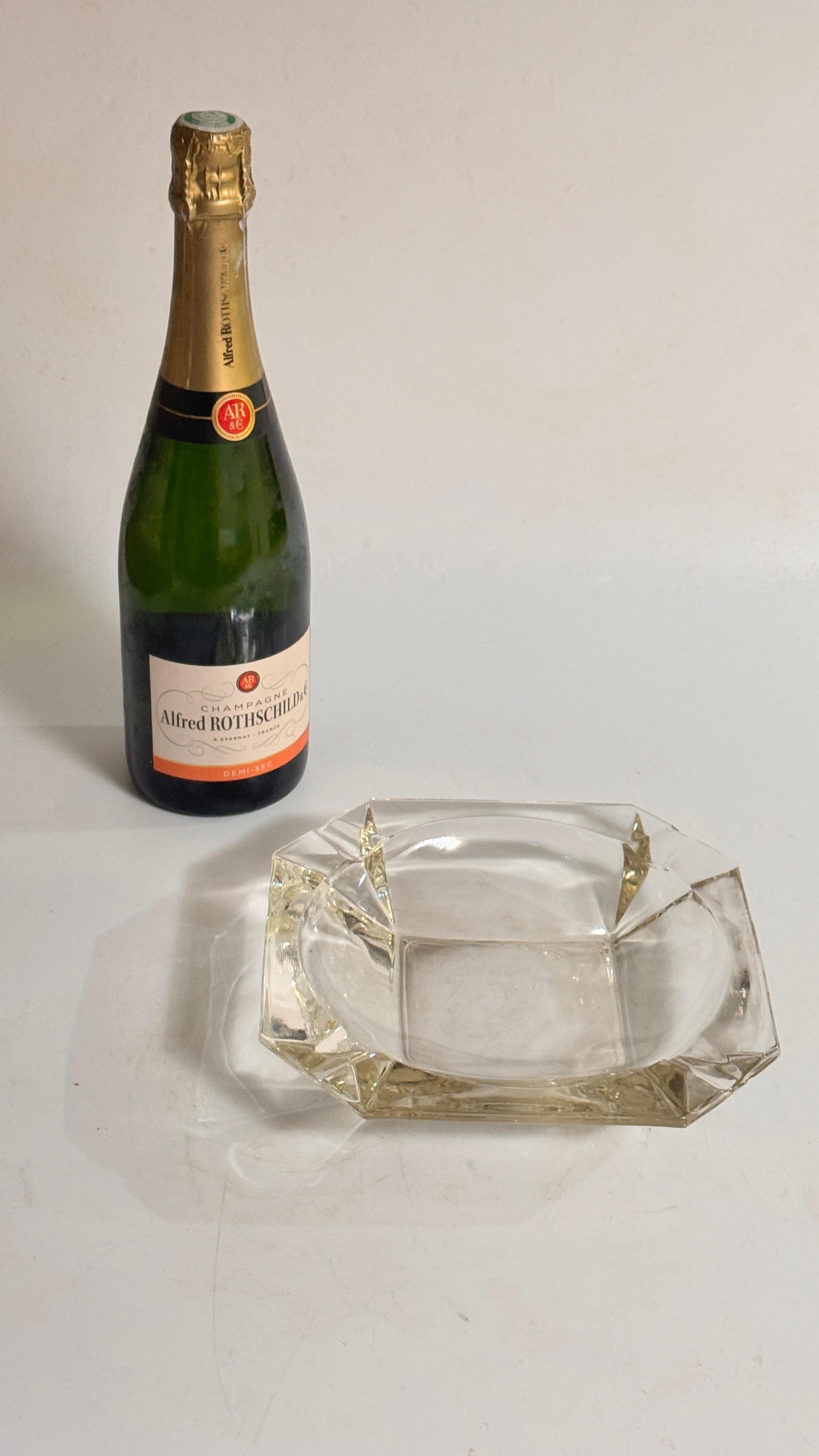 
Cet impressionnant cendrier en verre français des années 1970 présente une forme large et solide, façonnée avec de multiples facettes. Le verre est transparent mais présente de subtils reflets jaunes en fonction de la lumière, ce qui confère à la