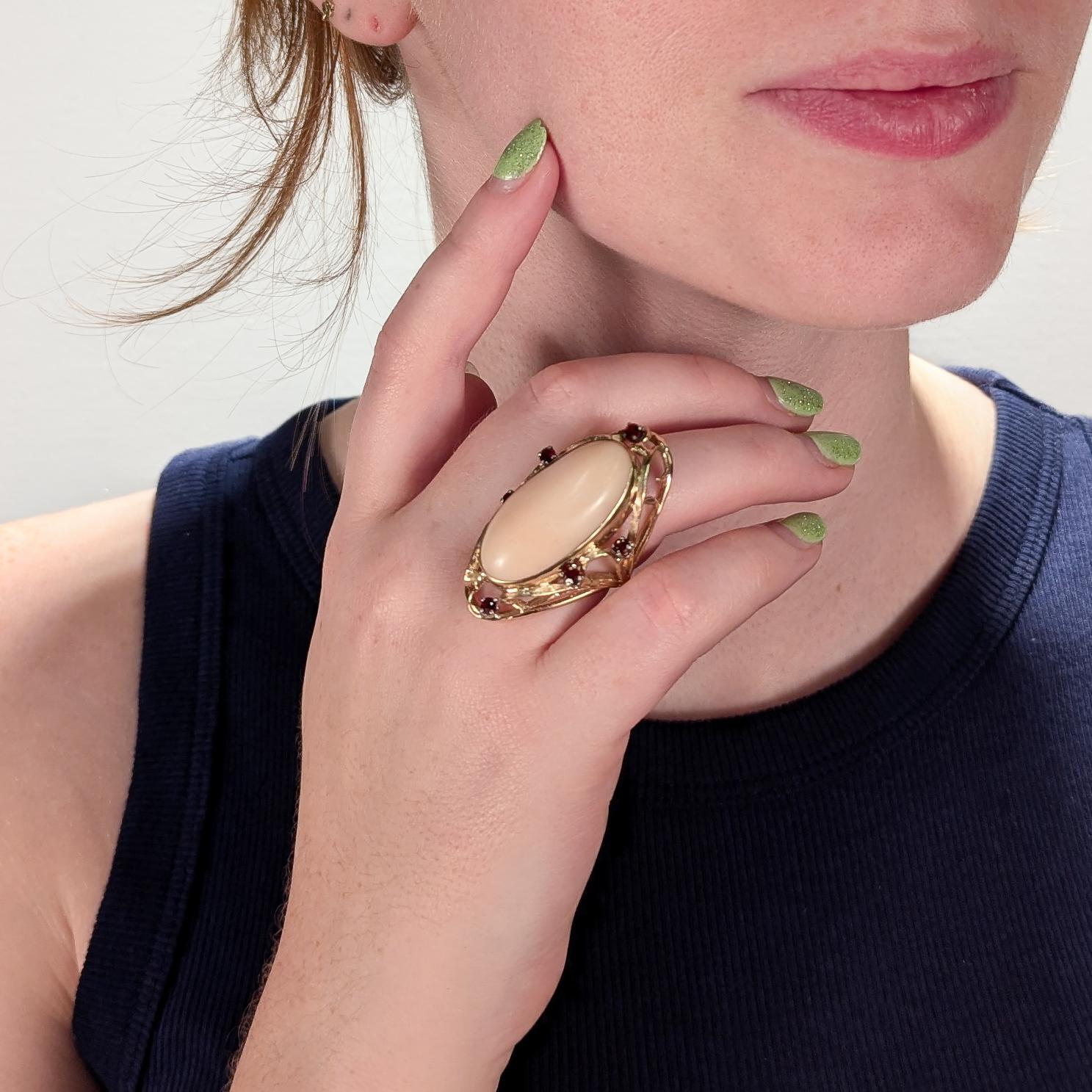 A fine 1970s handmade studio cocktail ring.

In 14k yellow gold.

Bezel set to the center with a very large angel skin coral cabochon in a sculptural, flowing organic mount interspersed with single cut garnet gemstones.

The mount's design leans