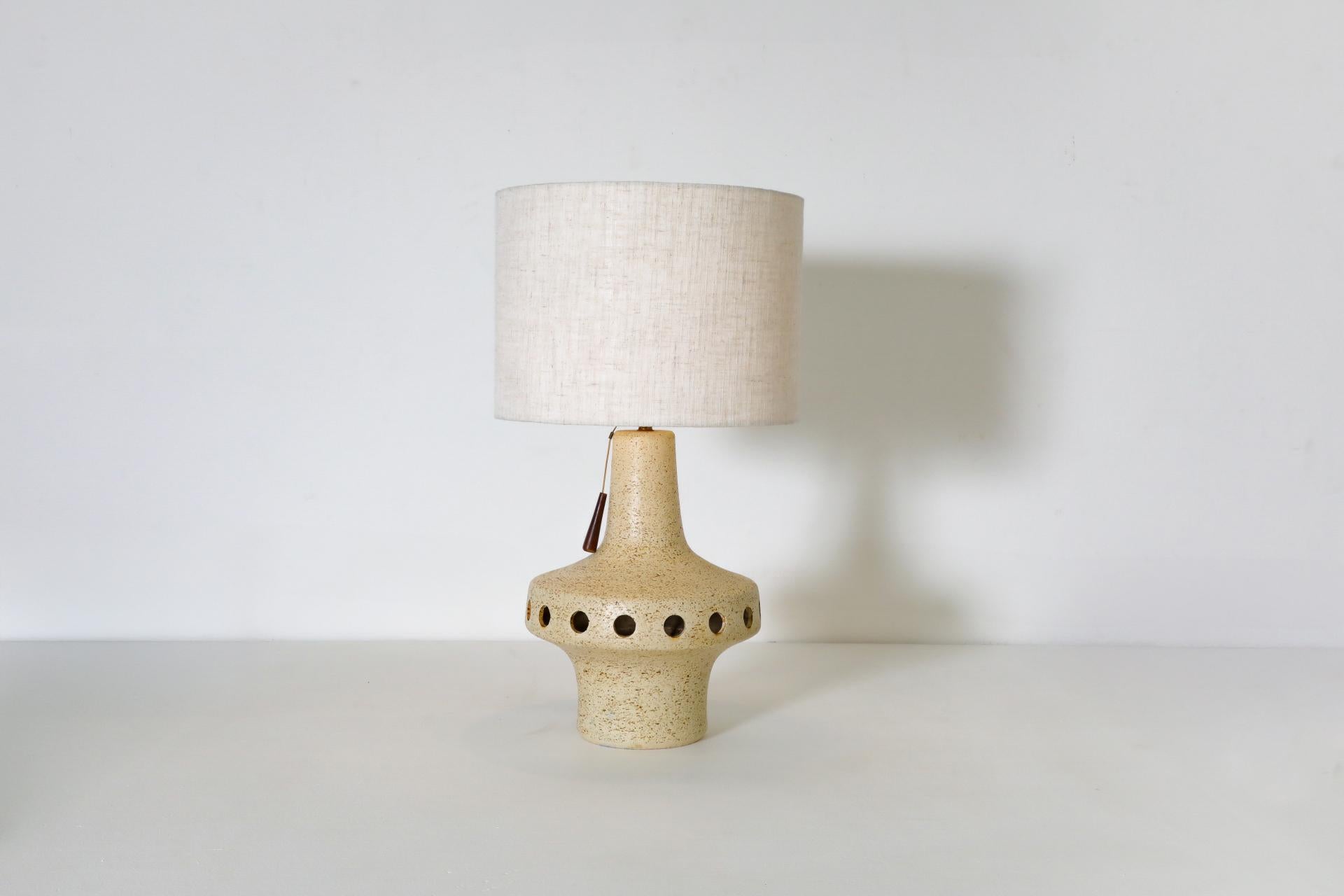 Large Space-Age UFO shaped ceramic table lamp with a speckled cream glaze, orbiting circle cut-outs and a beige patterned fabric shade which measures 14