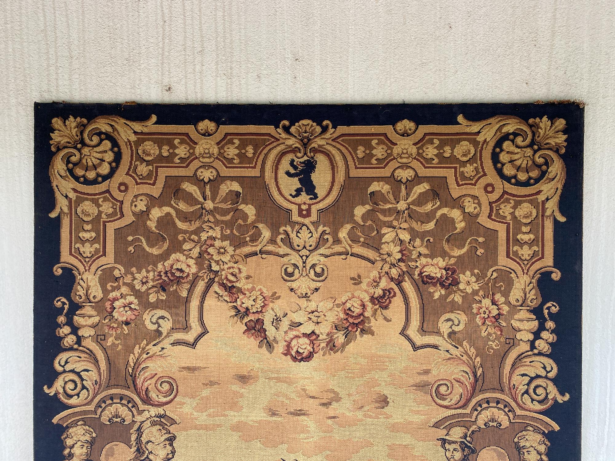 This is a 19th century machine woven tapestry in gold, black and burgundy threads featuring a large castle surrounded by figures and decorative imagery. The bottom edge has a name and manufacturer information and indicates it was made in Berlin. The