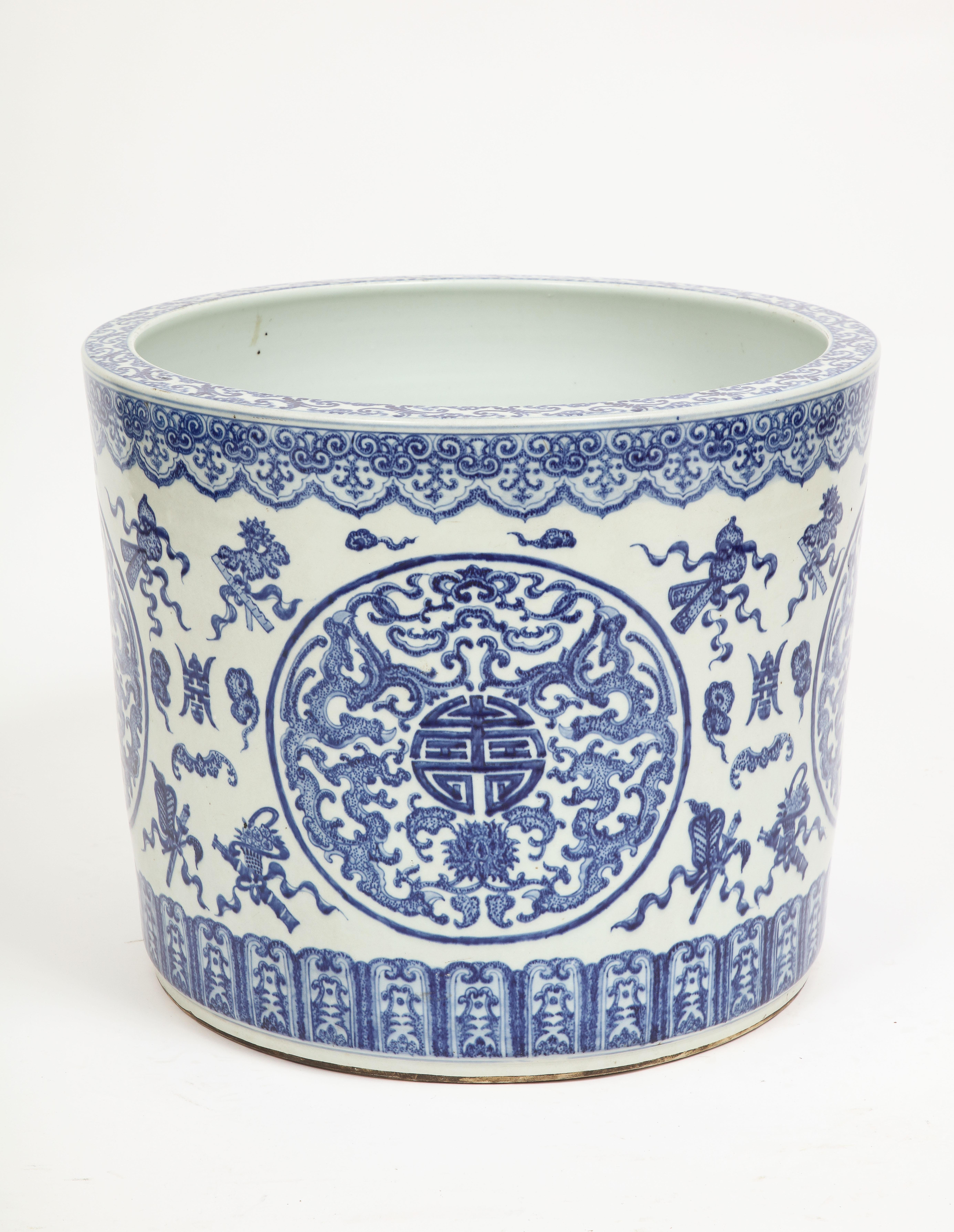 A Large 19th Century Chinese blue and white porcelain fishbowl/planter with Chinese Emblems and Designs. This piece is large and cylindrical in form with hand-painted blue over white designs of Chinese characters, emblems and upper and lower border