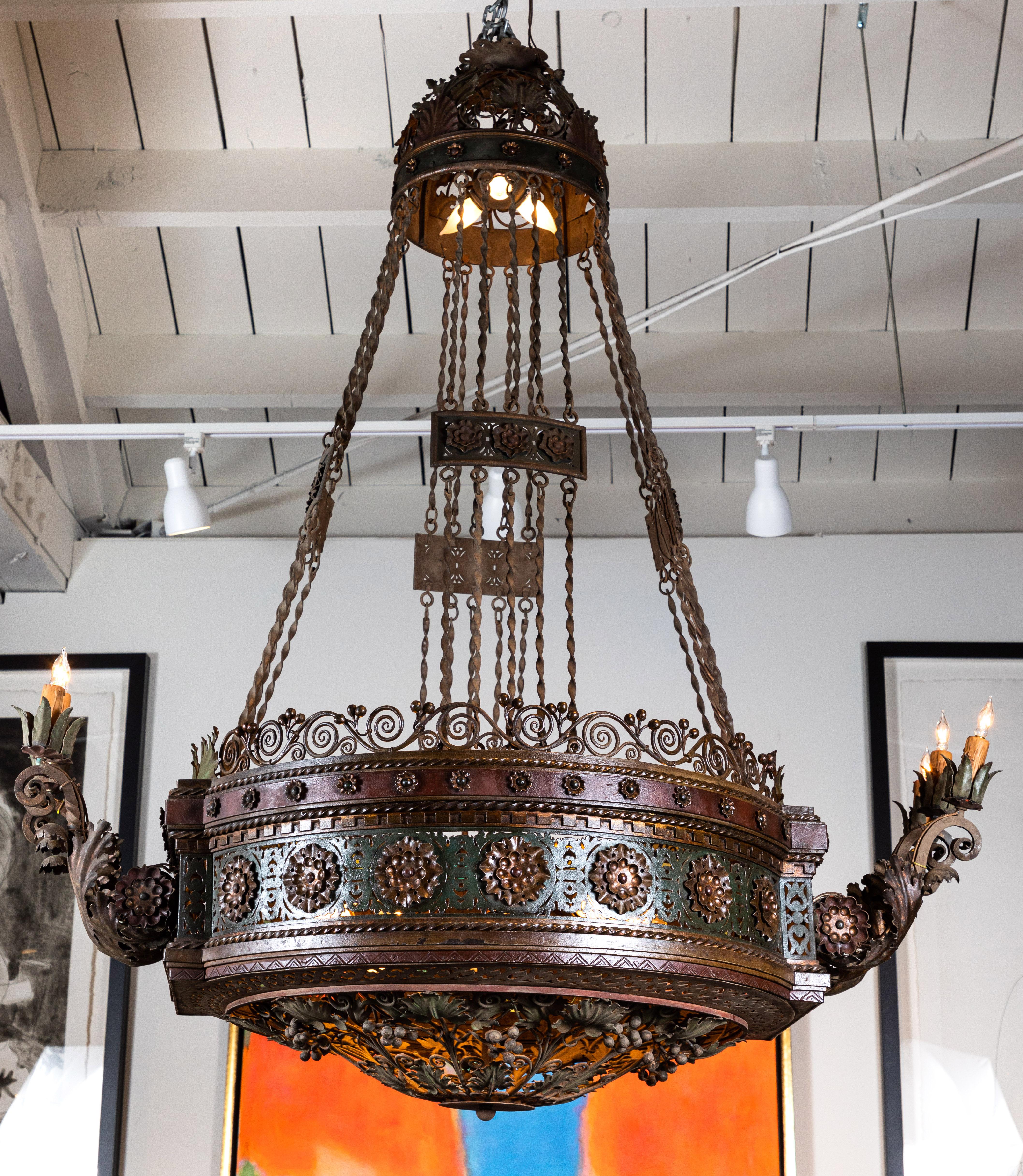 Absolutely grand, hand forged, patinated, chandelier featuring a circlet of foliate medallions and a series of six, serpentine, extruding candelabra. The remarkable, pierced basket holds another ten lights, and is comprised of a of intertwining