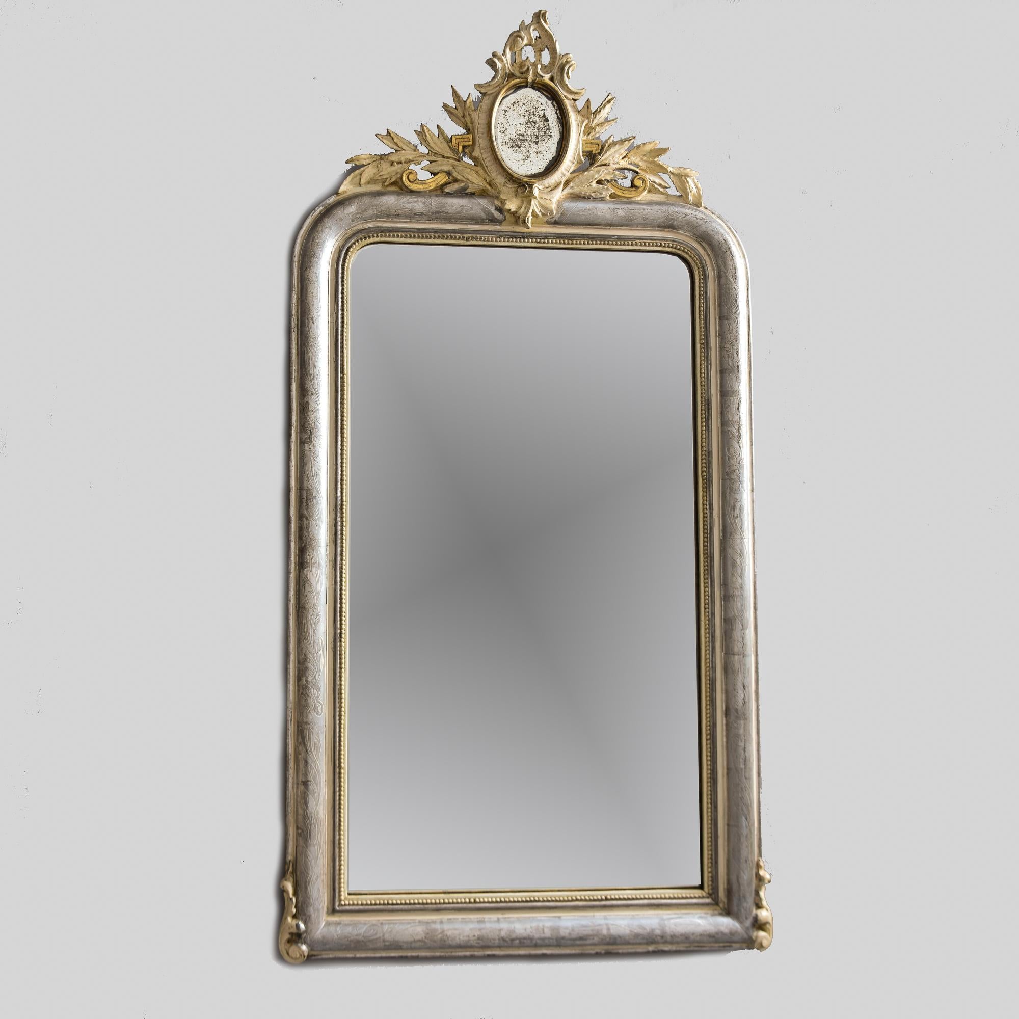 Found in France, this large Louis Philippe mirror dates from the 1870s. Silver gilt frame has subtle etched design of leaves and vines, contrasting gold leaf beaded trim on inner edge and giltwood crown with mirrored center. Giltwood details on