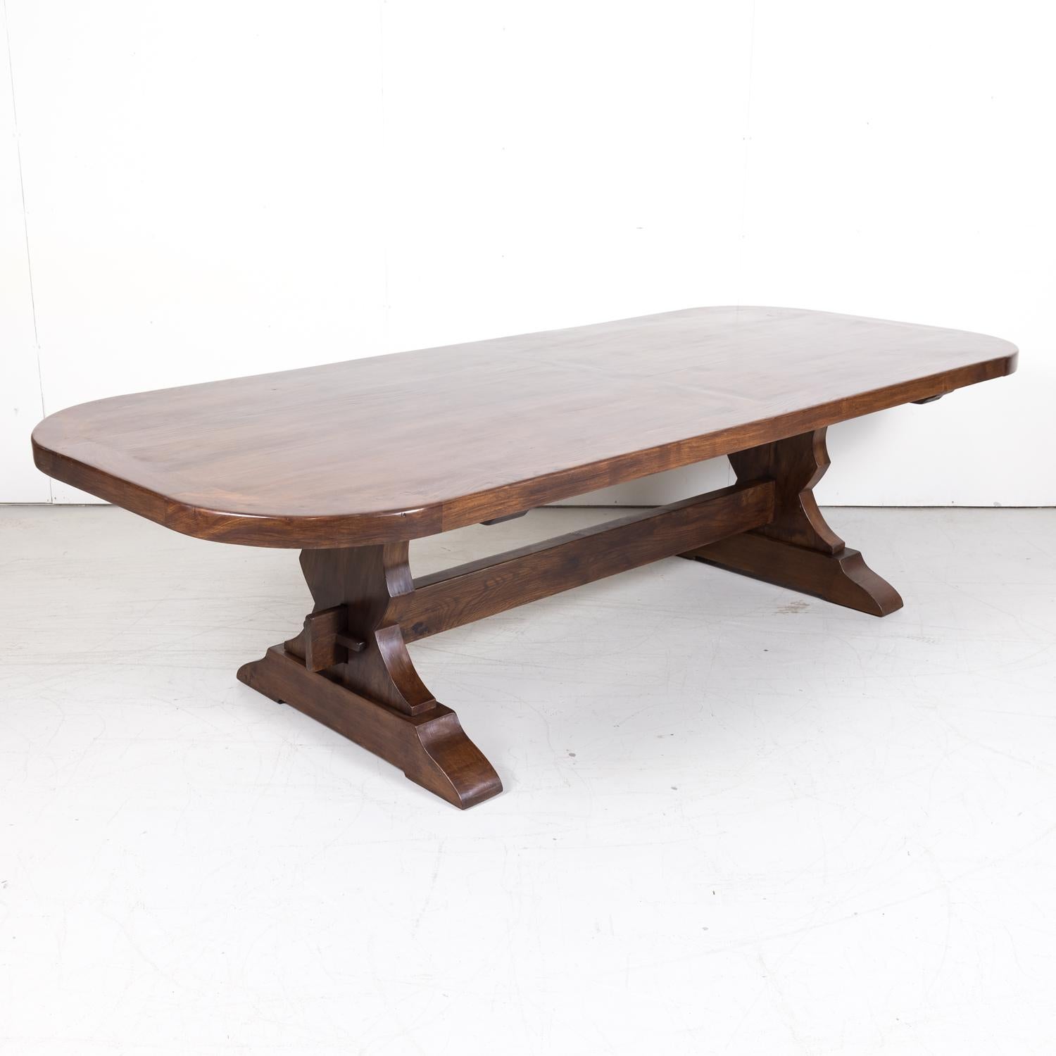 A late 19th century French trestle table handcrafted of solid chestnut in Provence, near Gordes, circa 1890s, having a thick inset plank top with a banded edge supported by two carved trestle bases joined by a center stretcher. This beautiful French