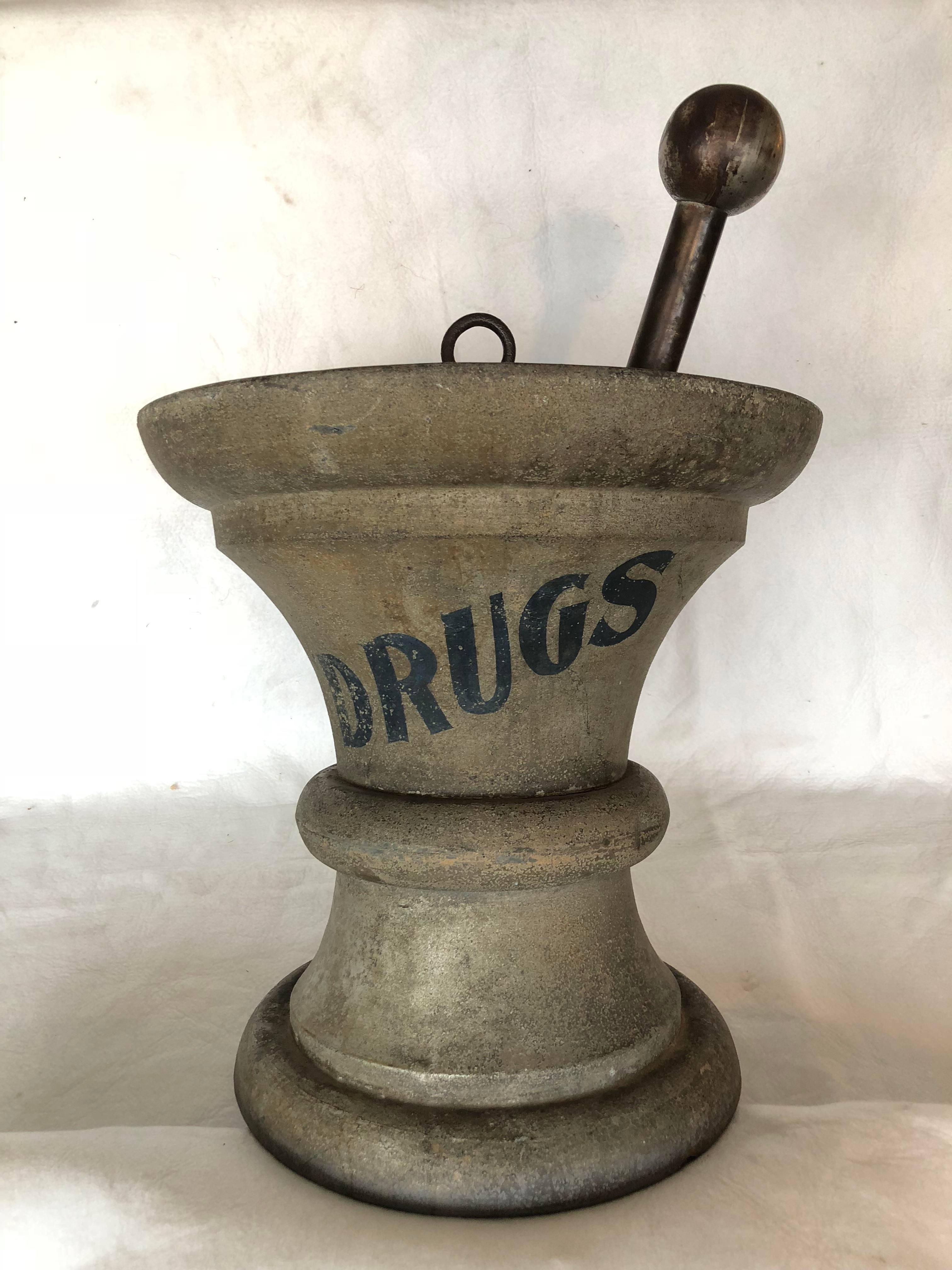 19th century apothecary trade sign in the form of a mortar and pestle in full round tin, finished in grey sand paint with word 'drugs' in black on the diagonal, central hanging loop, nickel-plated pestle knob, 18