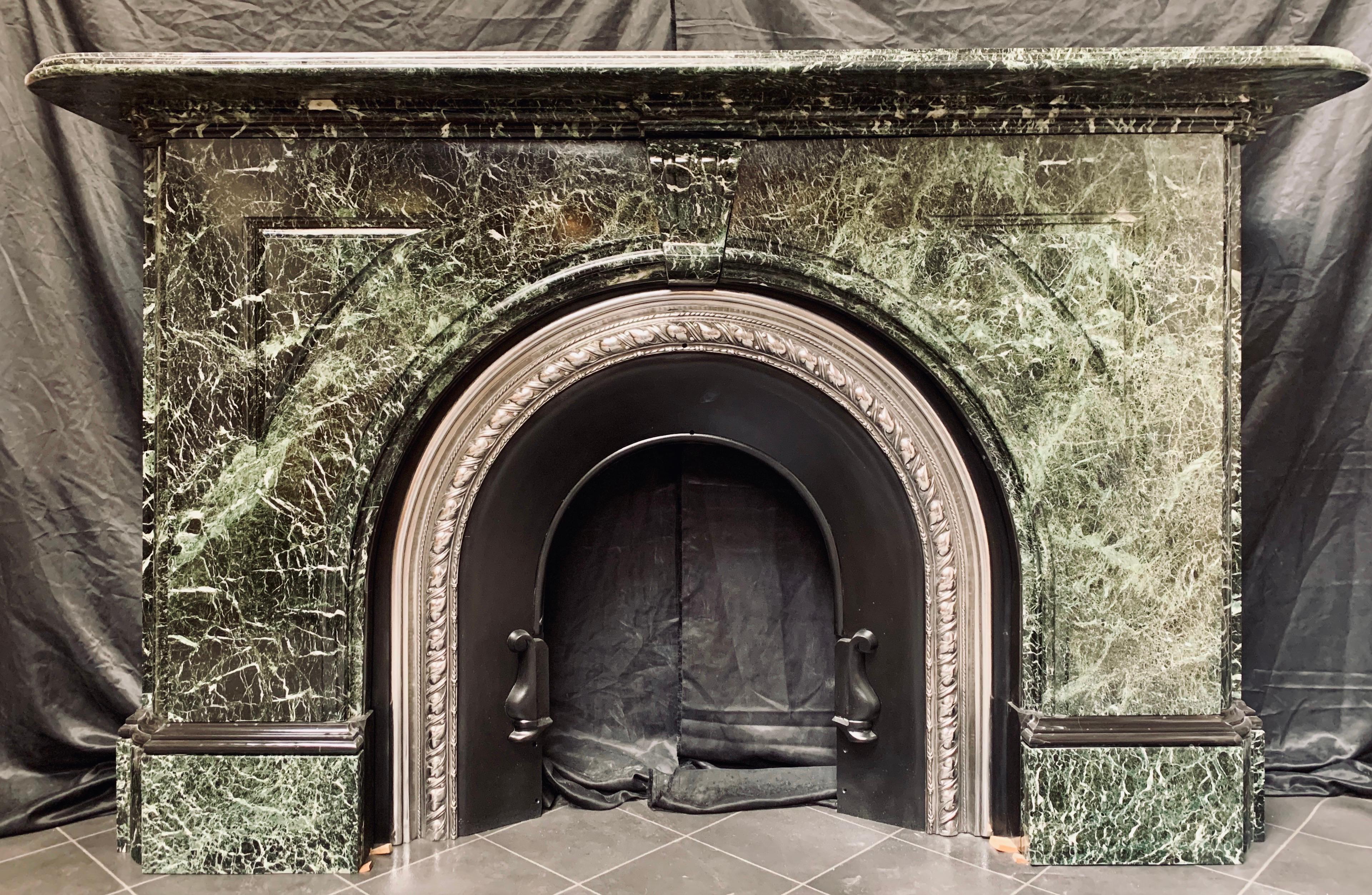 A large and masculine 19th century arched fireplace surround carved in rich vareated Verde Antico marble, a generous double thick bullnose shelf rests above a stepped and moulded under cornice, supported by a raised scalloped fluted keystone, and