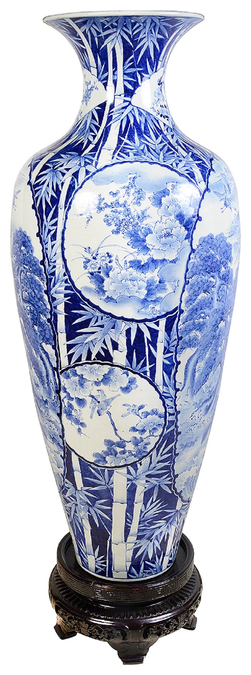 A large and impressive late 19th Century (Meiji period 1868-1912) Japanese blue and white vase on stand.
Having wonderful hand painted bamboo to the ground, with inset panels depicting mountainous scenes, blossom trees and flying cranes. mounted on