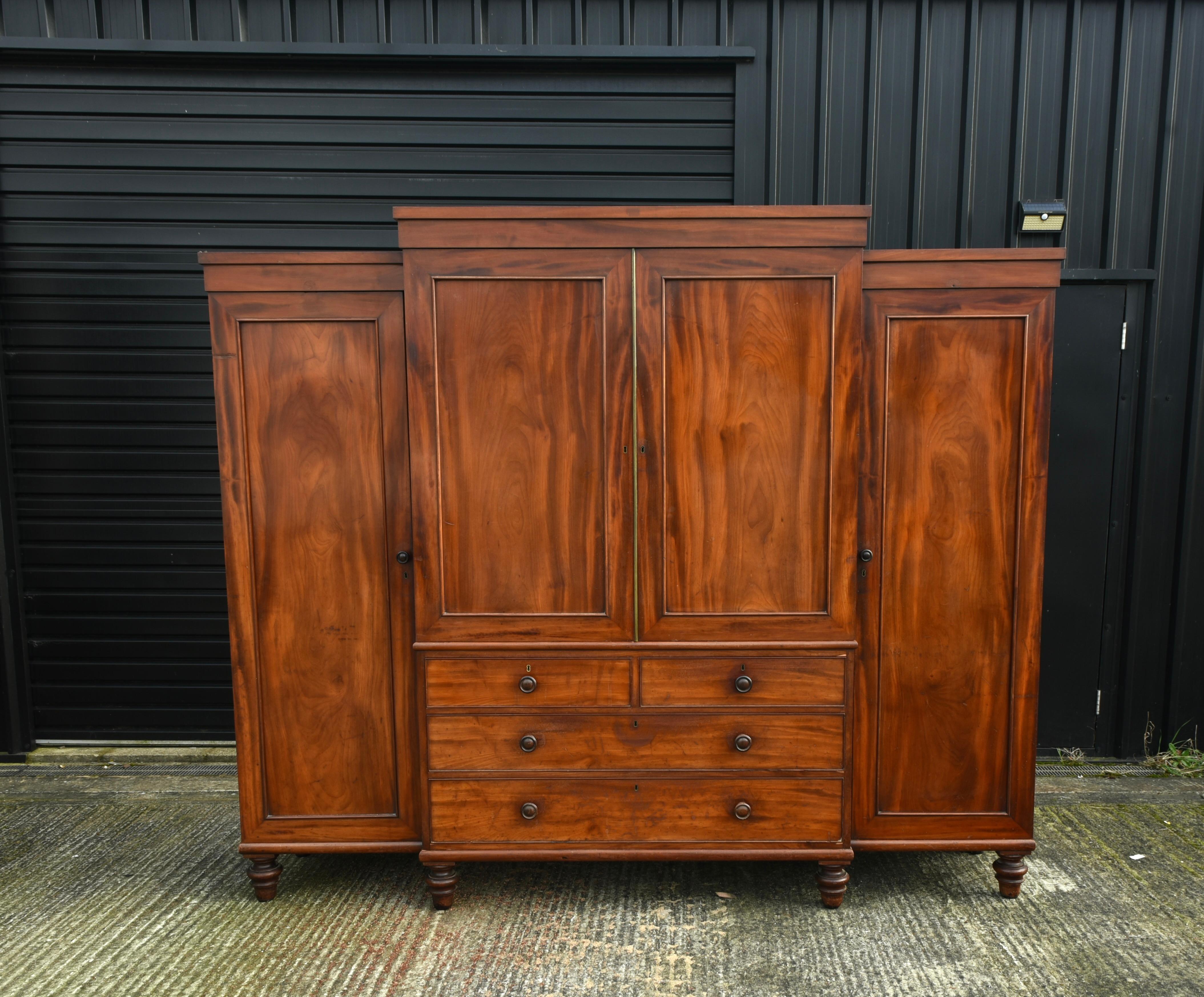 This is a large 19th Century (c.1830) antique mahogany breakfront wardrobe that is in great condition with a good grain and wonderful antique patina. It is constructed of solid mahogany and oak throughout. The centre section has 5 large slide out