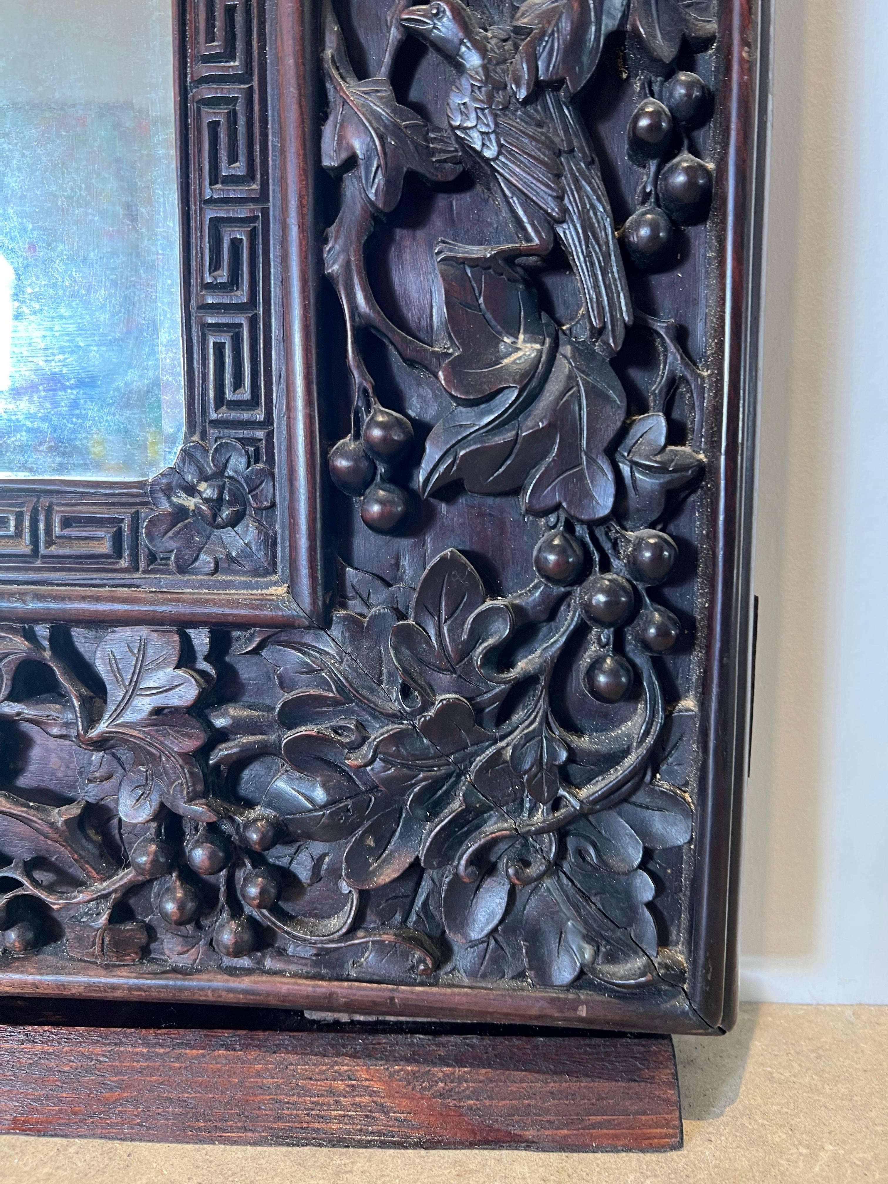 A 19th century deeply carved rosewood mirror in a very large scale from the Canton region of China. This large vertical mirror is fully carved with folliage, animals, birds berries and dragons. It is highly decorative and would be beautiful mixed