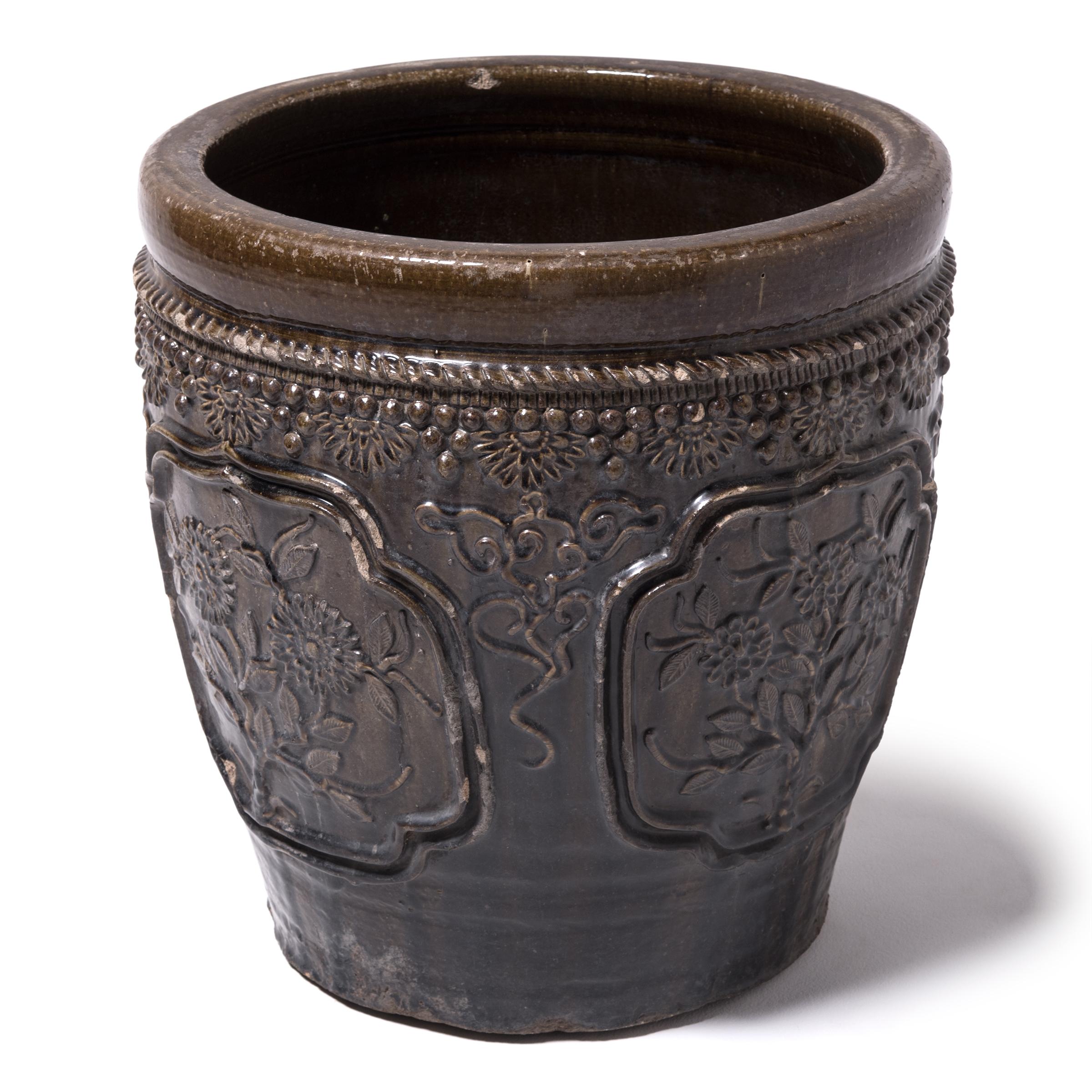 This large glazed jar was hand crafted in Shanxi province over a century ago. Masterfully crafted, the jar is patterned in high relief featuring medallions portraits of blooming flowers and trimmed around the rim with floral, bead and rope-like