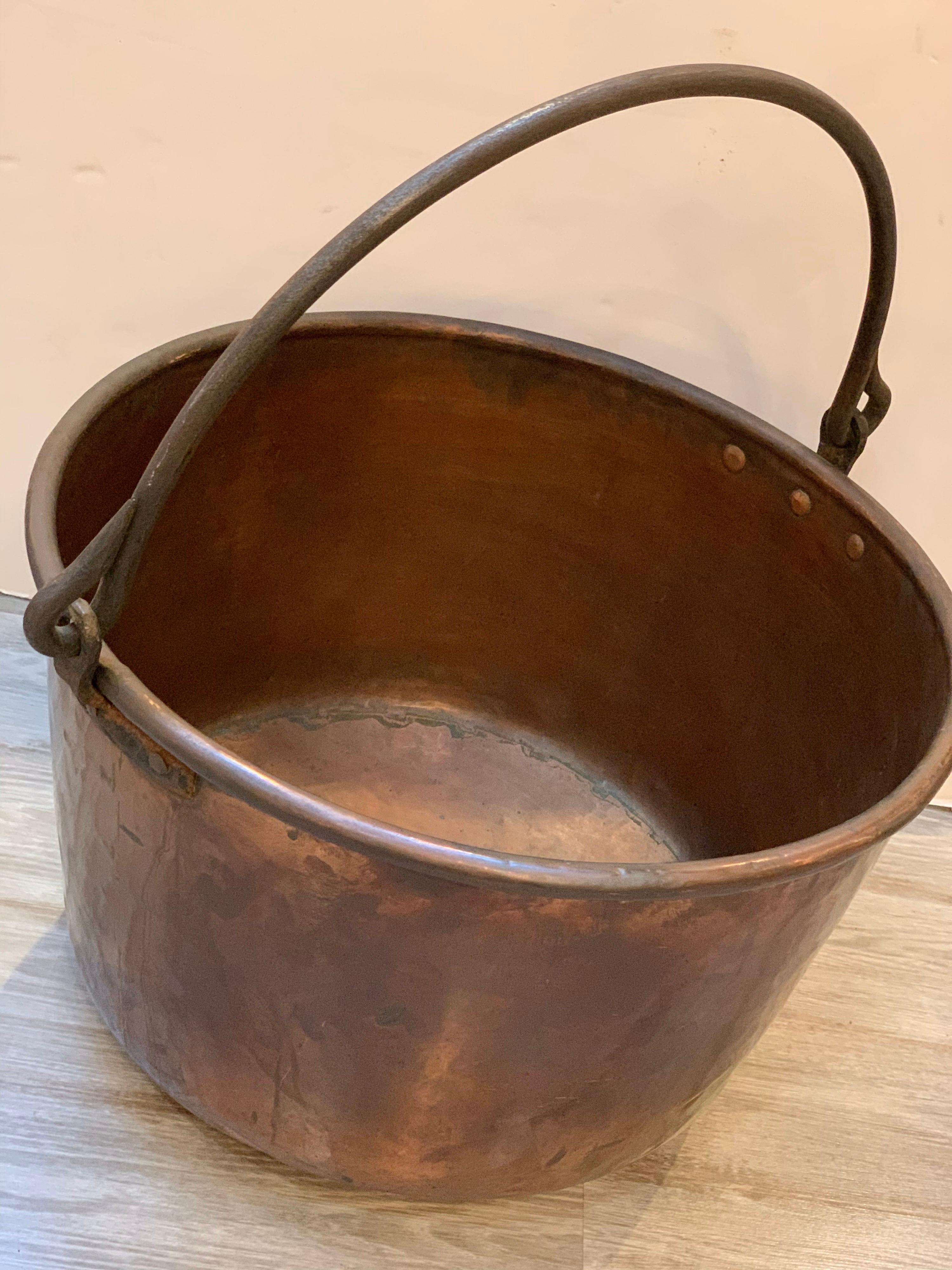 A large handmade copper and iron handled pot with rolled and rat tailed iron handle. 16 inches tall and the handle adds another 12 inches. Excellent for storing wood for the fireplace or a planter. A rare piece of antique handmade copper with
