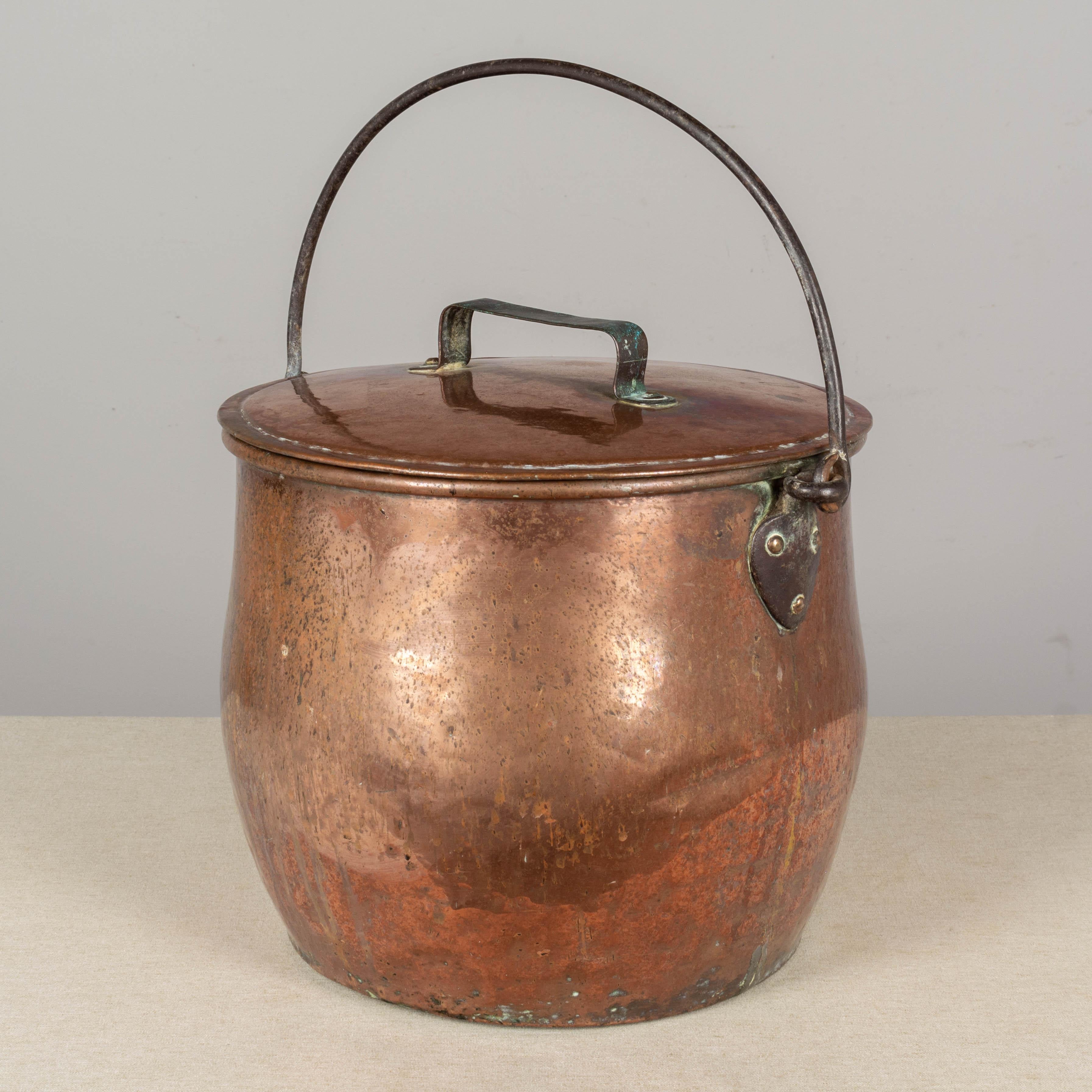 A large 19th century French hammered copper stock pot with tight fitting riveted handled lid. Hand-wrought iron loop to hang the pot over a fire. Beautiful warm patina with streaks and green oxidation. Rustic condition with dents and light