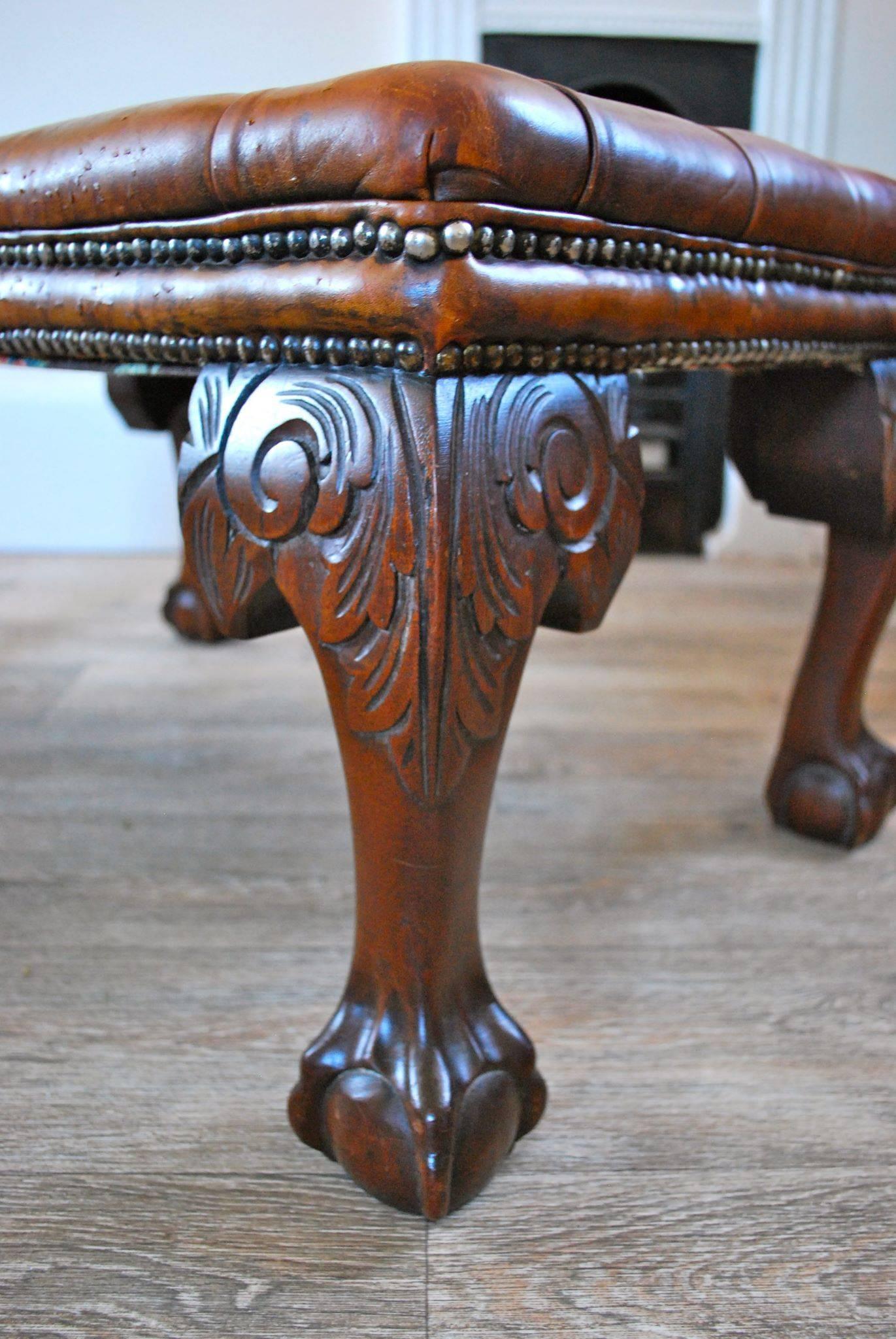 A large 19th century deep buttoned leather foot stool.
This stool consist of a deep buttoned leather top with two rows brass dome-head nails standing on four heavy carved legs leading down to ball and claw feet.