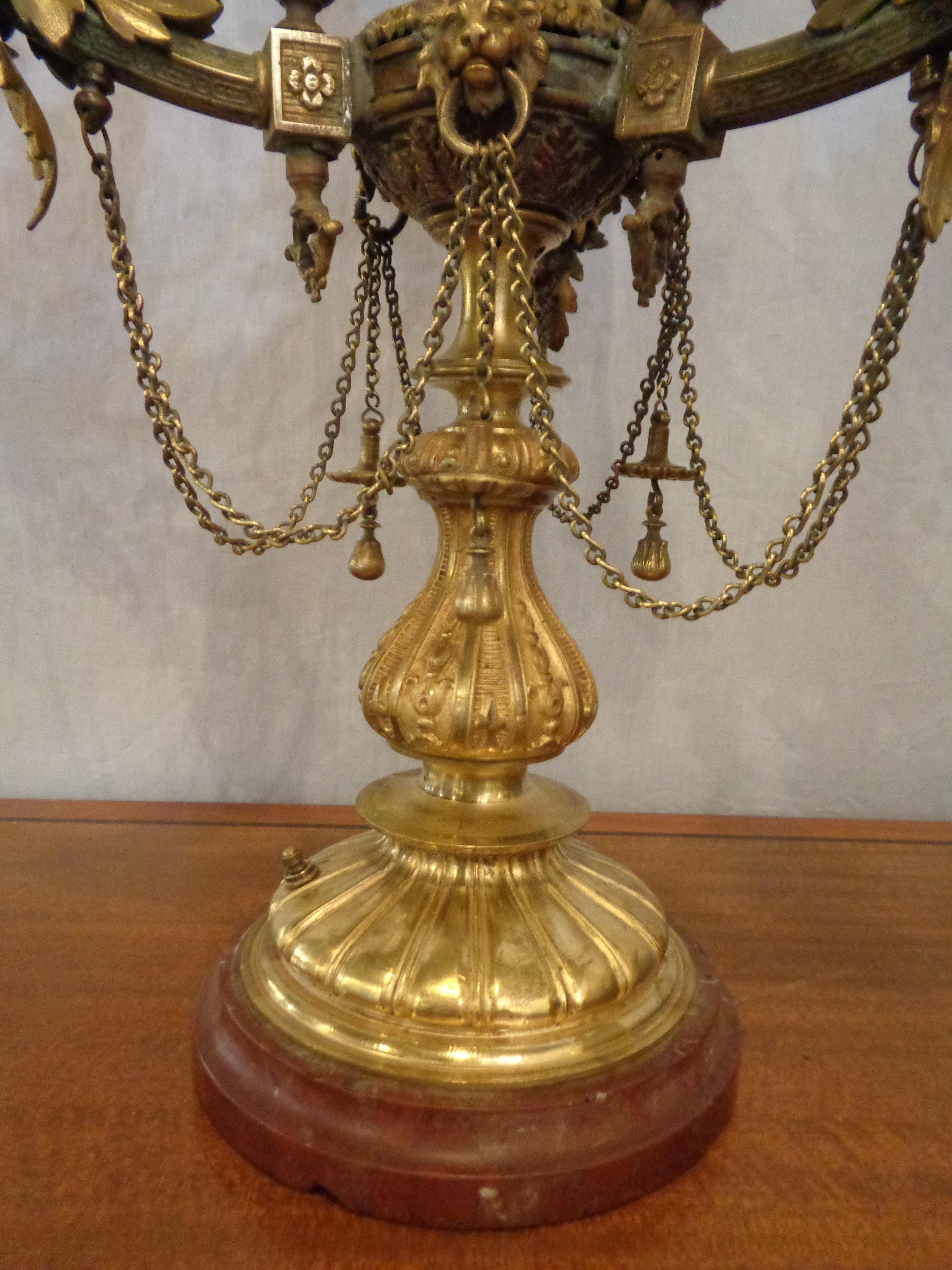 A large doré bronze full bodied serpent candelabra lamp. The rouge marble base supporting a group of three full bodied dragons in flight seemingly chained to a central post decorated by a centre pole and lion heads. The whole terminating in three