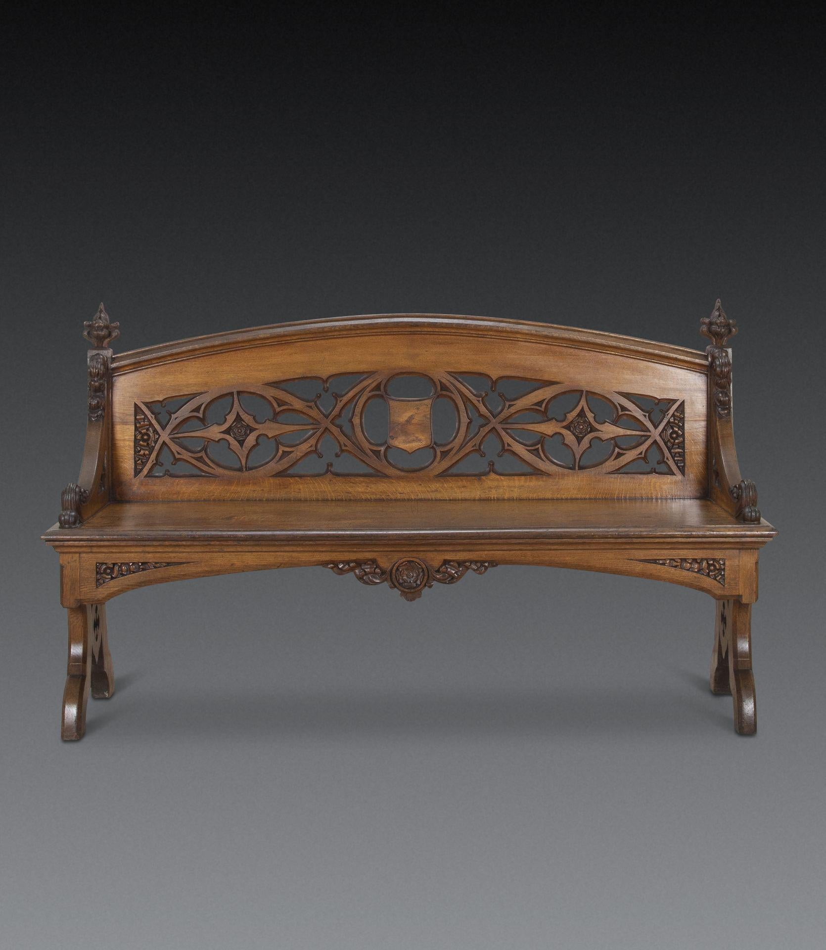 A large C19th oak hall bench, with arched back with pierced carving featuring intertwined trifold and quatrefoils, flanked by swept arms with scroll corbels and coronet capitals, raised on a moulded seat with pierced carved supports, chamfered edges