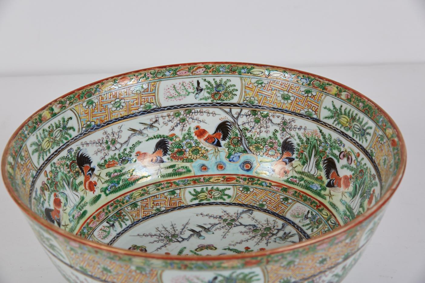 A large 19th century famille verte Chinese export porcelain punch bowl with banded polychrome decoration of roosters in a landscape reflected on the interior and exterior of the bowl. Narrow bands of fruit and foliage motifs, some on a gilt