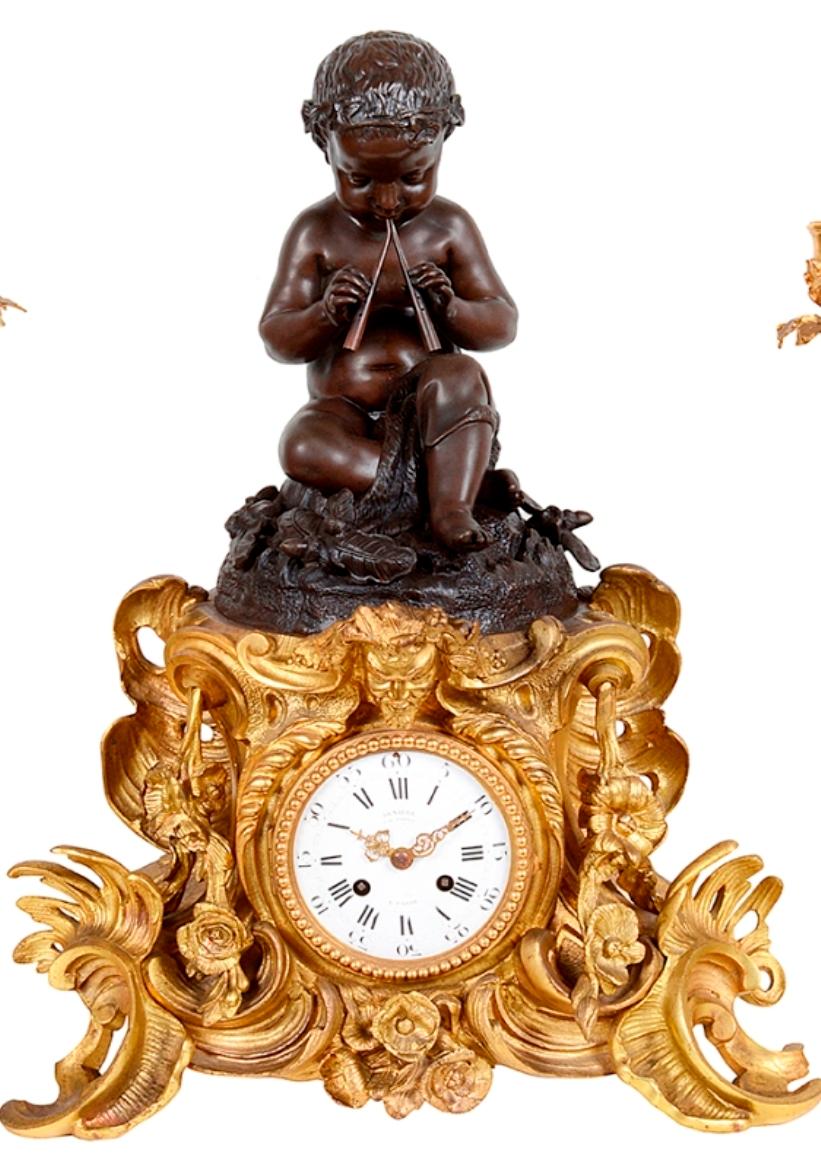 An enchanting 19th century French gilded ormolu and patinated bronze Louis XVI style clock garniture.
The four branch, Rococo influenced candelabra each supported by three classical putti. 
The clock with a bronze seated boy playing the pipes,