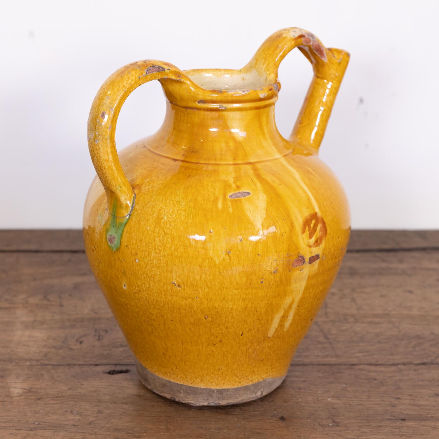 A large 19th century French water jug or cruche orjol from the Languedoc region in southwest France, having a mustard yellow glaze with green and caramel colored drips and two beautifully arched handles that rise above the opening with the spout