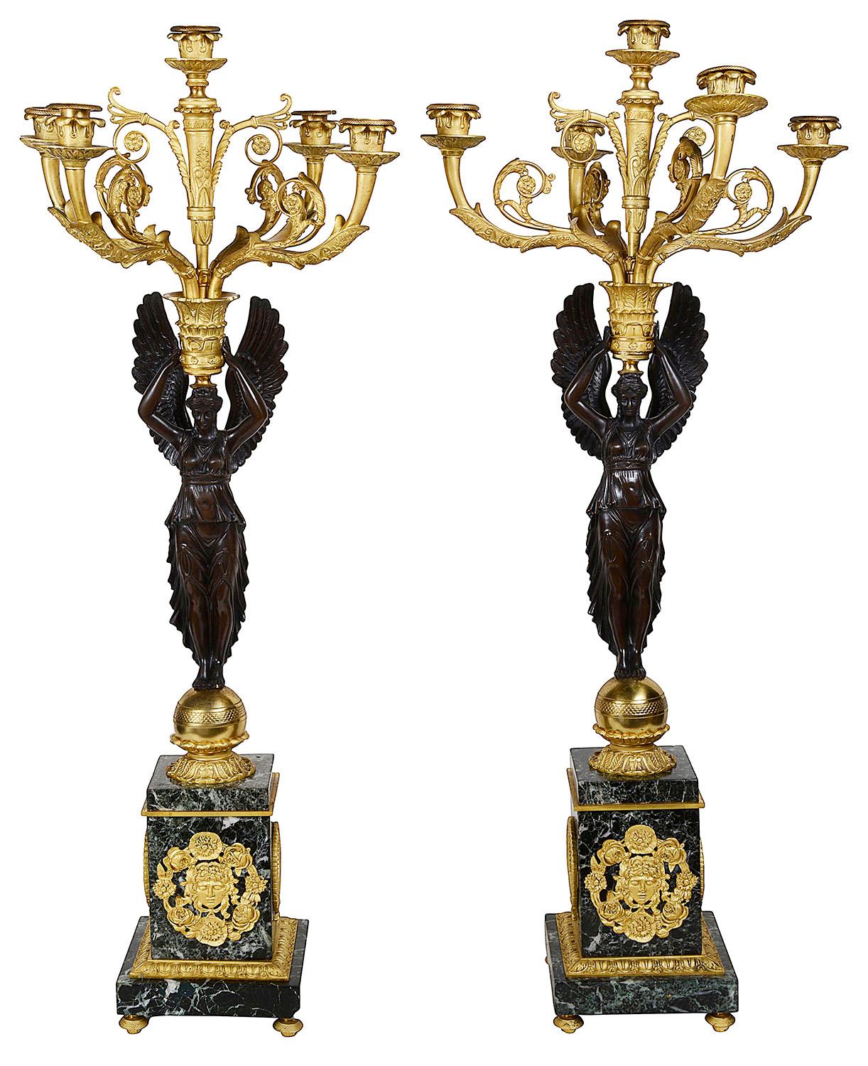 A very impressive and fine quality 19th century French Empire influenced clock set. Having a pair of winged female figures supporting five branch candelabra with scrolling foliate decoration, raised on gilded globes and green marble plinths with