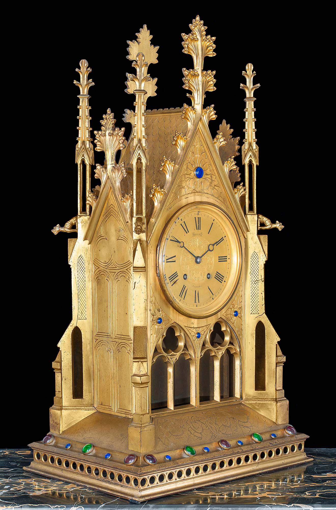 An impressive and large late 19th century French quarter chiming gilt brass Gothic Revival bracket or mantel clock retailed by Hall & Company, Manchester. The case, with engraved floral decoration and applied coloured cabuchon jewel mounts, encloses
